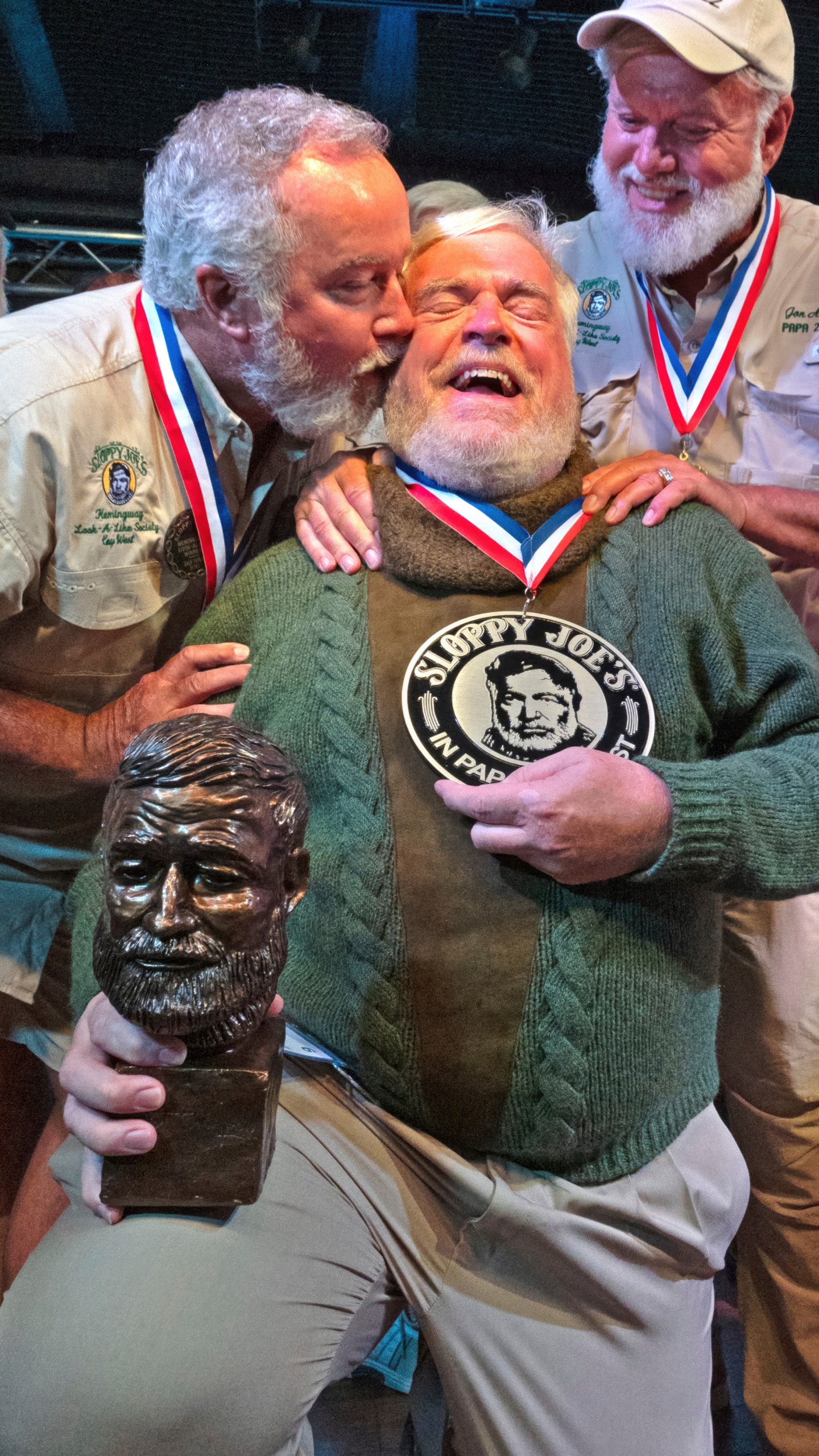 In this Saturday, July 22, 2023, photo provided by the Florida Keys News Bureau, Zach Taylor, left, and Jon Auvil, right, congratulate Gerrit Marshall, center, for winning the annual Hemingway Look-Alike Contest at Sloppy Joe's Bar in Key West, Fla. After 11 years of competing Marshall, a Madison, Wisc., resident, finally achieved success on his 68th birthday. The competition was a highlight of the annual Hemingway Days festival that ends Sunday, July 23. Ernest Hemingway lived in Key West throughout most of the 1930s. Taylor won in 2021, while Auvil was the 2022 winner. (Andy Newman/Florida Keys News Bureau via AP)