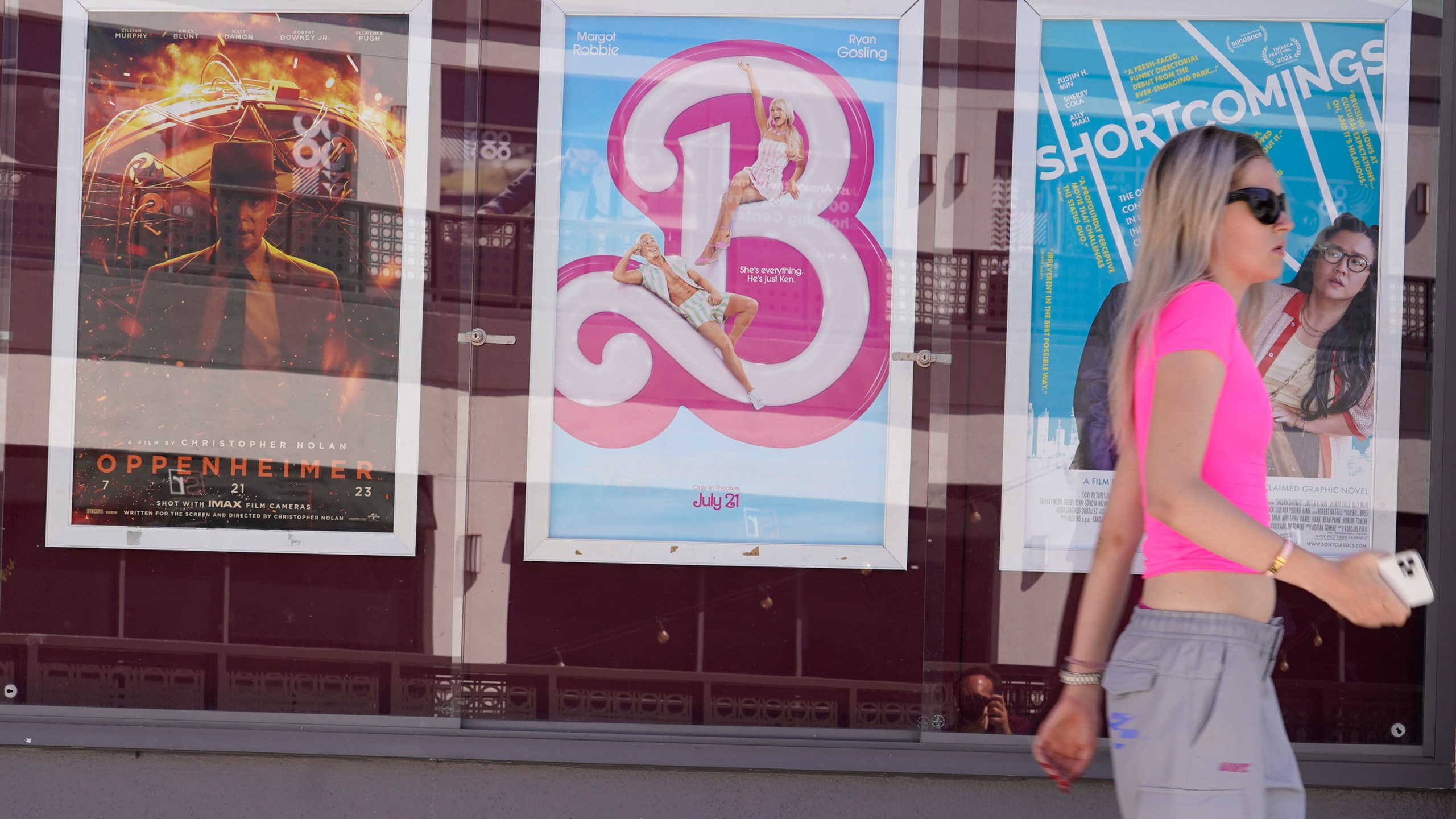 A woman walks past advertisements for the films "Oppenheimer," from left, and "Barbie," on Thursday, July 20, 2023, at the Landmark Theater in Los Angeles. (AP Photo/Chris Pizzello)