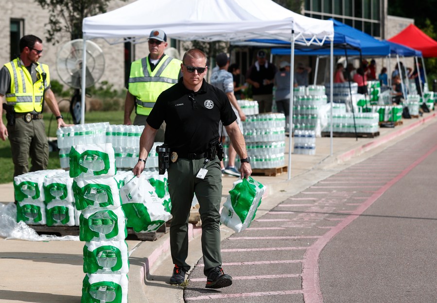 A police officer helps hand out bottled water to residents on Monday, July 24, 2023 at Forest Hill Elementary School in Germantown, Tenn. Residents of the Tennessee city were told that diesel fuel spilled into a local reservoir, and to avoid drinking tap water. People remain under an order Wednesday, July 26 to avoid using water for everything except flushing toilets. They can’t drink or boil tap water, or use it showering or bathing. (Mark Weber/Daily Memphian via AP)