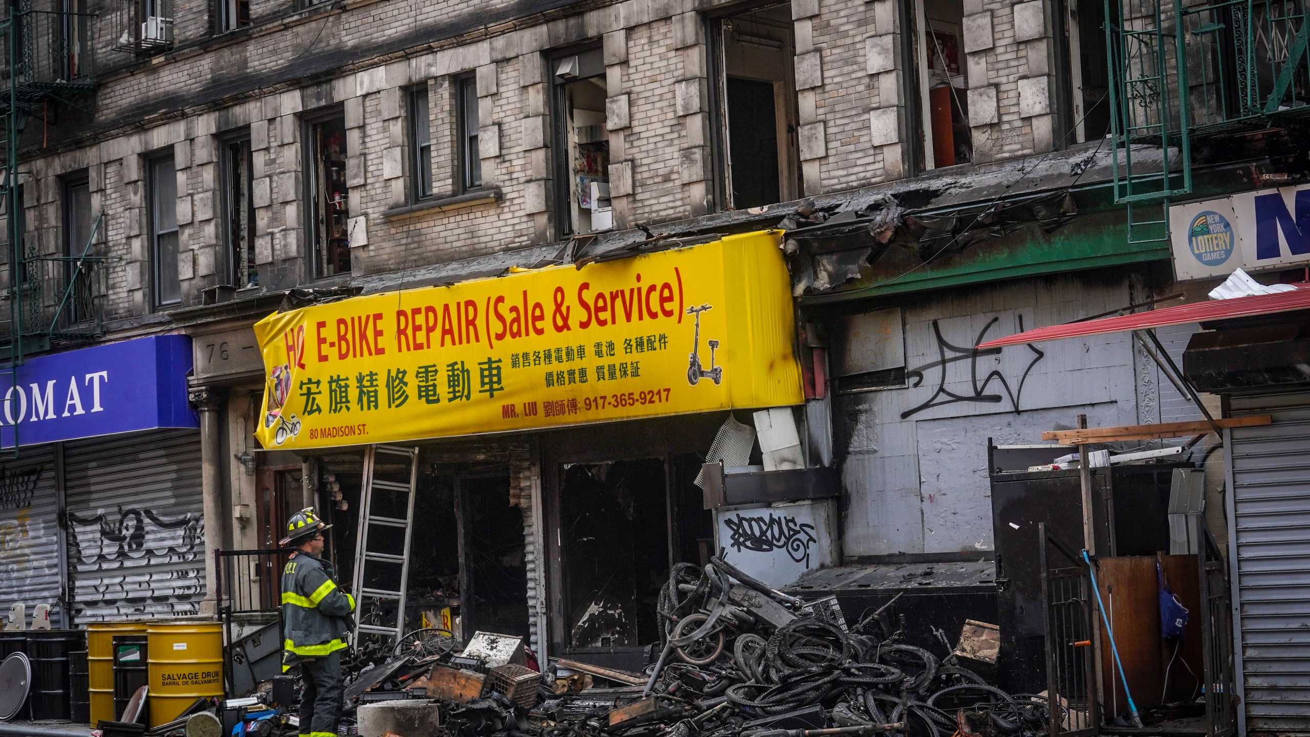 FILE - A firefighter looks through debris in the aftermath of a fire which authorities say started at an e-bike shop and spread to upper-floor apartments, Tuesday June 20, 2023, in New York. Federal officials are looking into cracking down on defective lithium-ion batteries that power hoverboards, scooters and motorized bicycles because of a rash of deadly fires caused by exploding batteries. The effort comes as New York City implements new laws meant to reduce the number of fires, injuries and deaths in a city where e-bikes have become ubiquitous.(AP Photo/Bebeto Matthews, File)