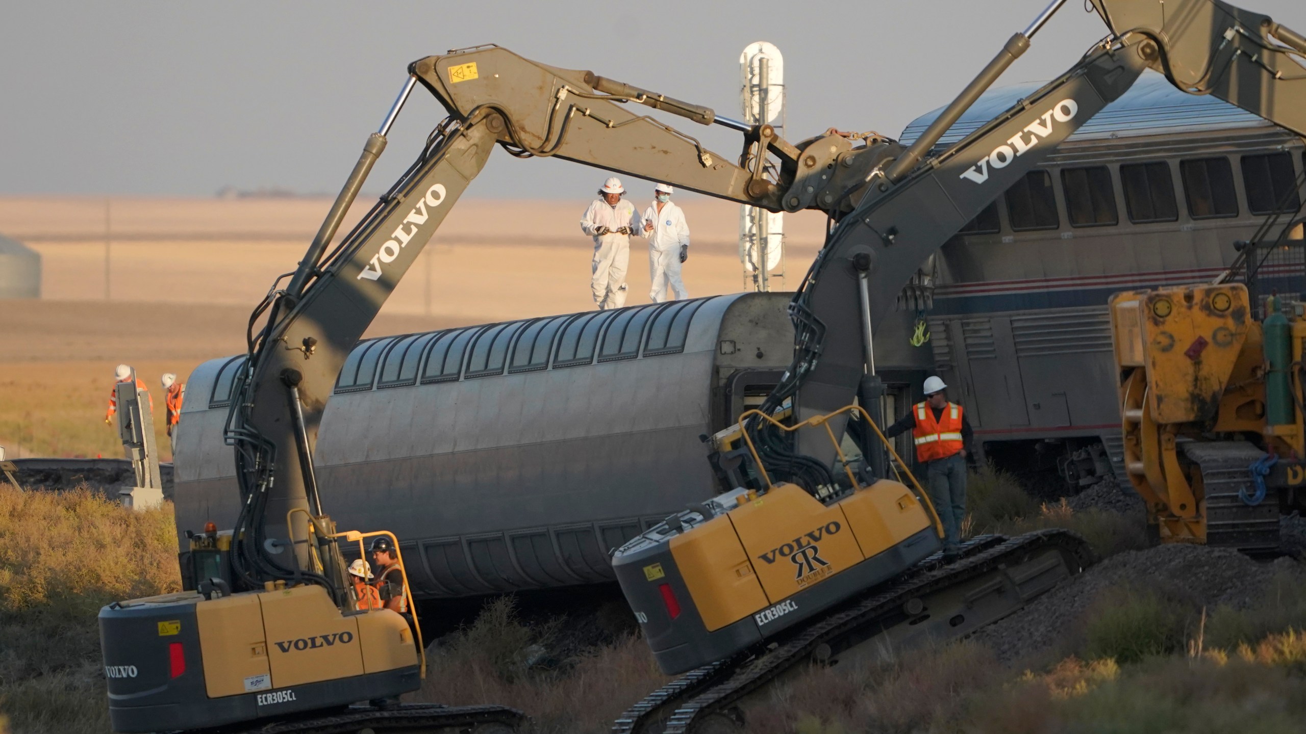 FILE - Workers stand on a train car on its side as front-loaders prop up another train car, Sept. 26, 2021, from an Amtrak train that derailed the day prior just west of Joplin, Mont., killing three people and injuring 49 others. The westbound Empire Builder was en route to Seattle from Chicago with two locomotives and 10 cars when it derailed. The derailment was caused by a combination of track issues, including wear and railbed instability, the National Transportation Safety Board said on Thursday, July 27, 2023. (AP Photo/Ted S. Warren, File)