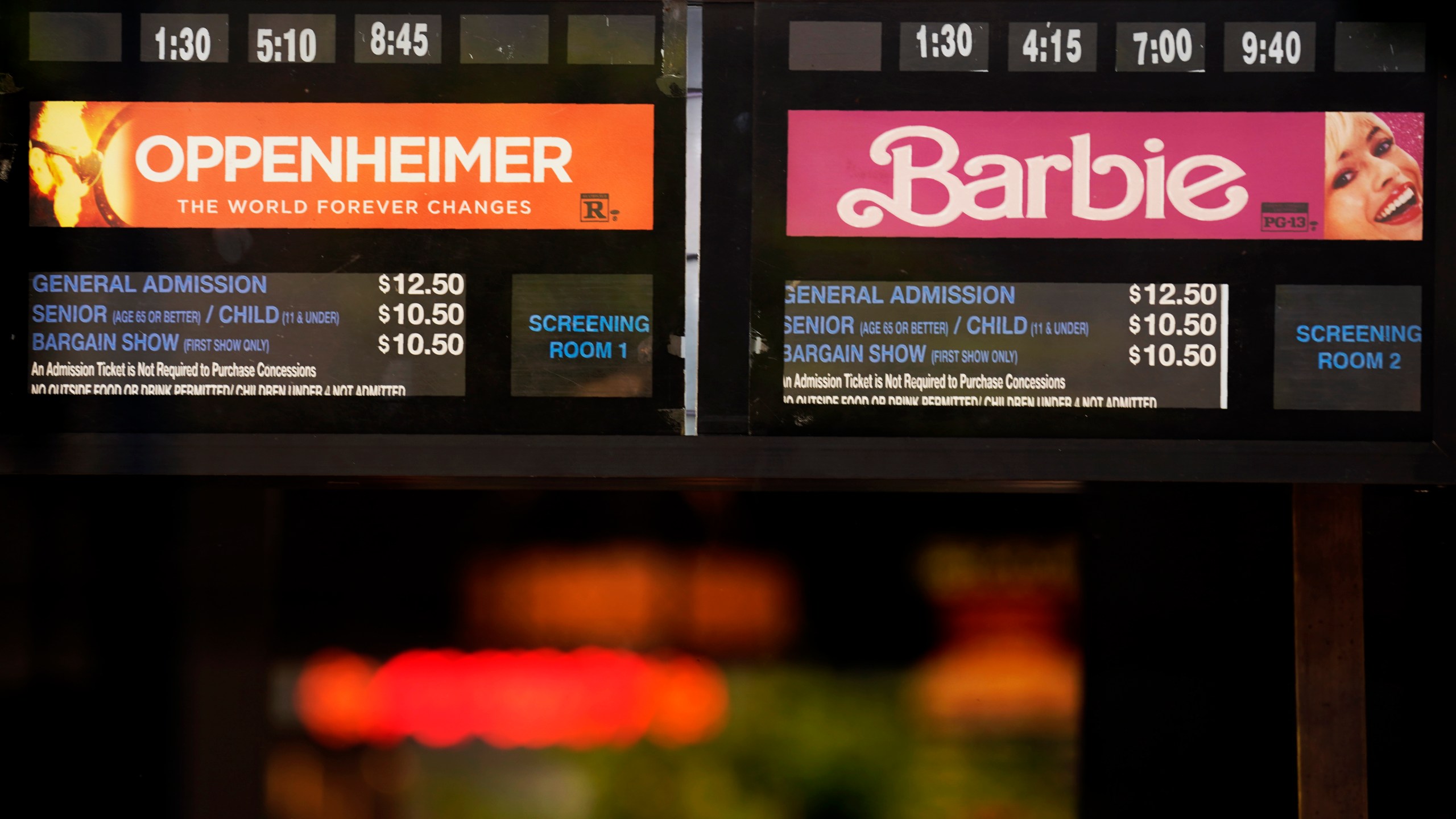 Showtimes for the films "Oppenheimer" and "Barbie" are pictured behind the box office window at the Los Feliz Theatre, Friday, July 28, 2023, in Los Angeles. (AP Photo/Chris Pizzello)