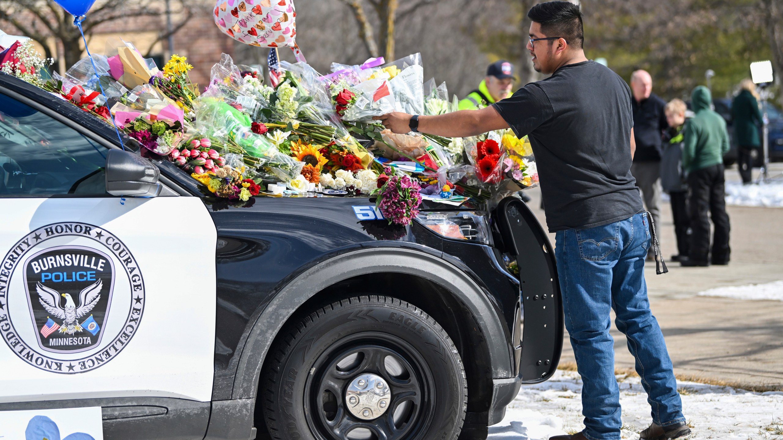 Crasto Cruz Reyes of Austin, Minn., places flowers at one of the three memorial vehicles in front of the Burnsville Police Department in Burnsville, Minn., Monday, Feb. 19, 2024. Two police officers and a firefighter who responded to a domestic situation at a suburban Minneapolis home were killed early Sunday during a standoff by a heavily armed man who shot at police from the home where seven children were also inside. (Craig Lassig/Pioneer Press via AP)