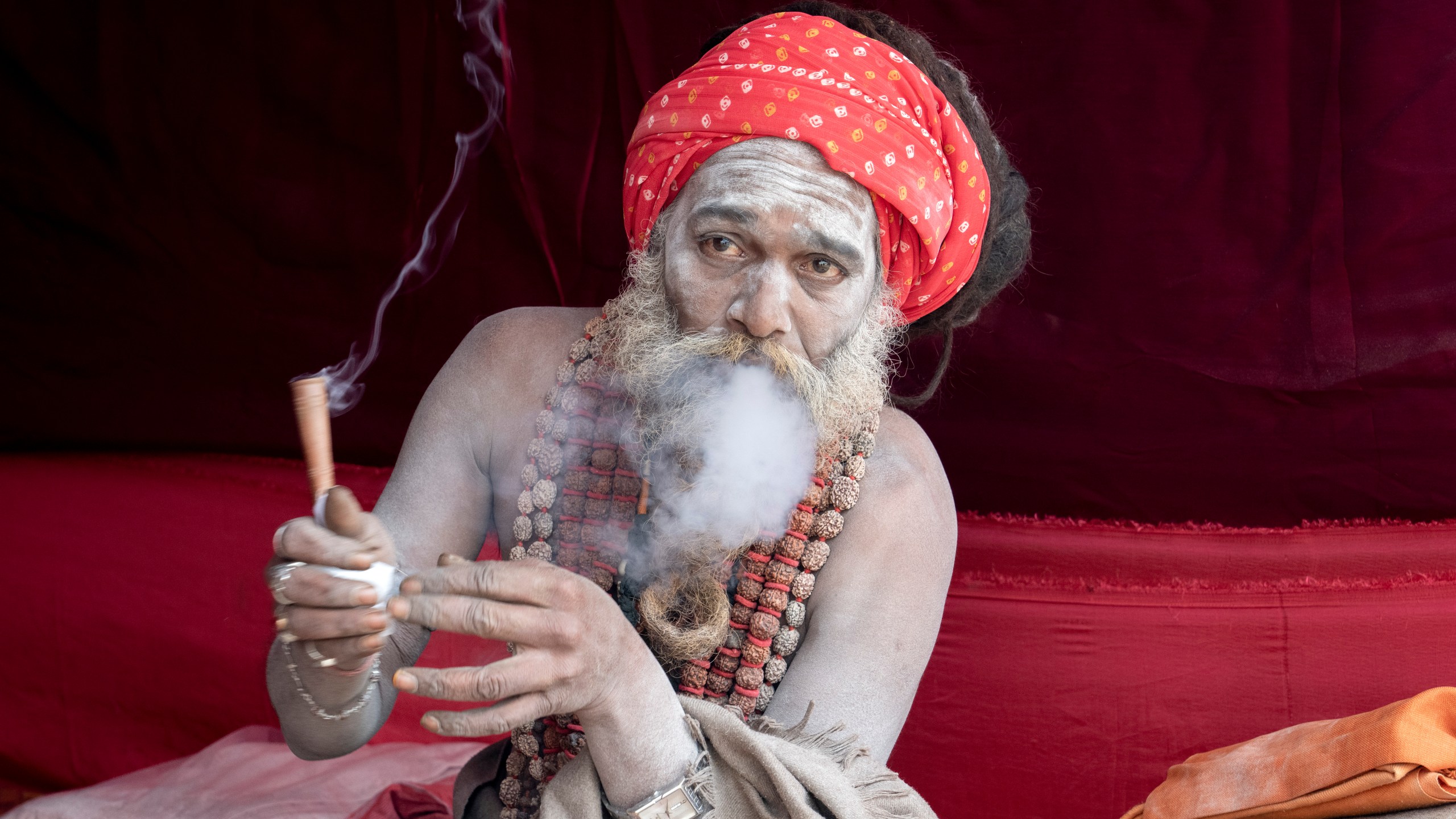 A Hindu holy man smokes marijuana at his makeshift living quarters at the confluence of the Ganges, the Yamuna and the mythical Saraswati rivers, a day before the official beginning of the 45-day-long Maha Kumbh festival, in Prayagraj, India, Sunday, Jan. 12, 2025. (AP Photo/Ashwini Bhatia)