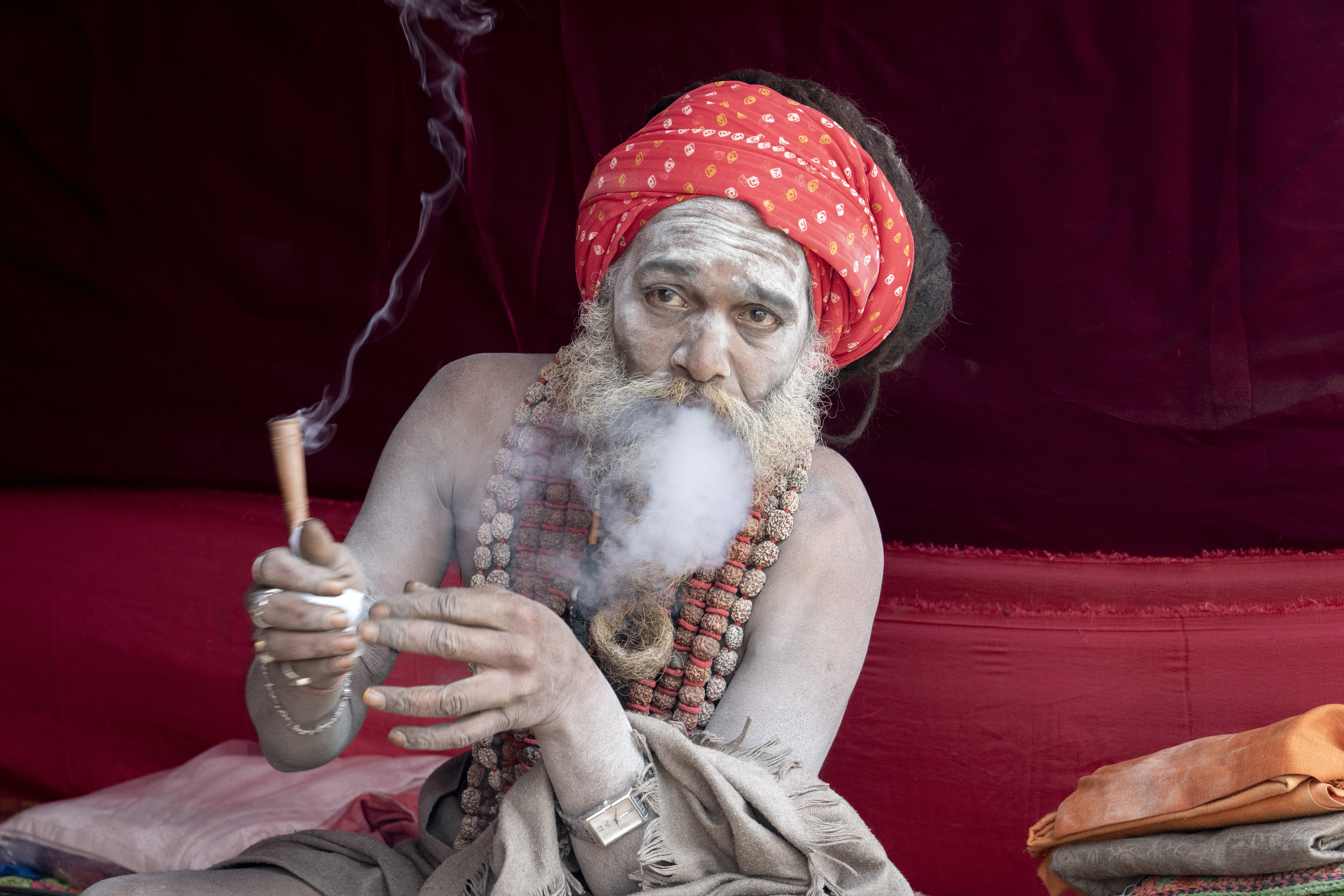 A Hindu holy man smokes marijuana at his makeshift living quarters at the confluence of the Ganges, the Yamuna and the mythical Saraswati rivers, a day before the official beginning of the 45-day-long Maha Kumbh festival, in Prayagraj, India, Sunday, Jan. 12, 2025. (AP Photo/Ashwini Bhatia)