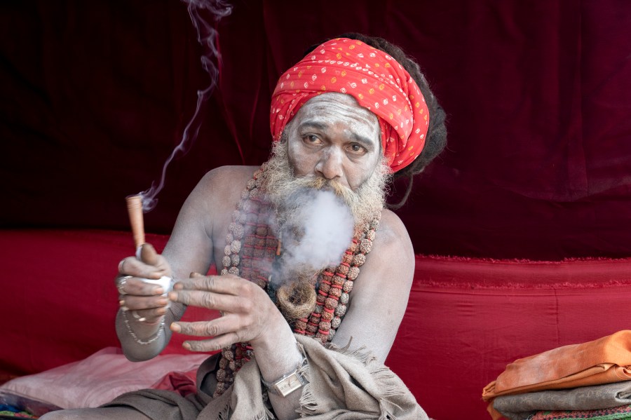 A Hindu holy man smokes marijuana at his makeshift living quarters at the confluence of the Ganges, the Yamuna and the mythical Saraswati rivers, a day before the official beginning of the 45-day-long Maha Kumbh festival, in Prayagraj, India, Sunday, Jan. 12, 2025. (AP Photo/Ashwini Bhatia)