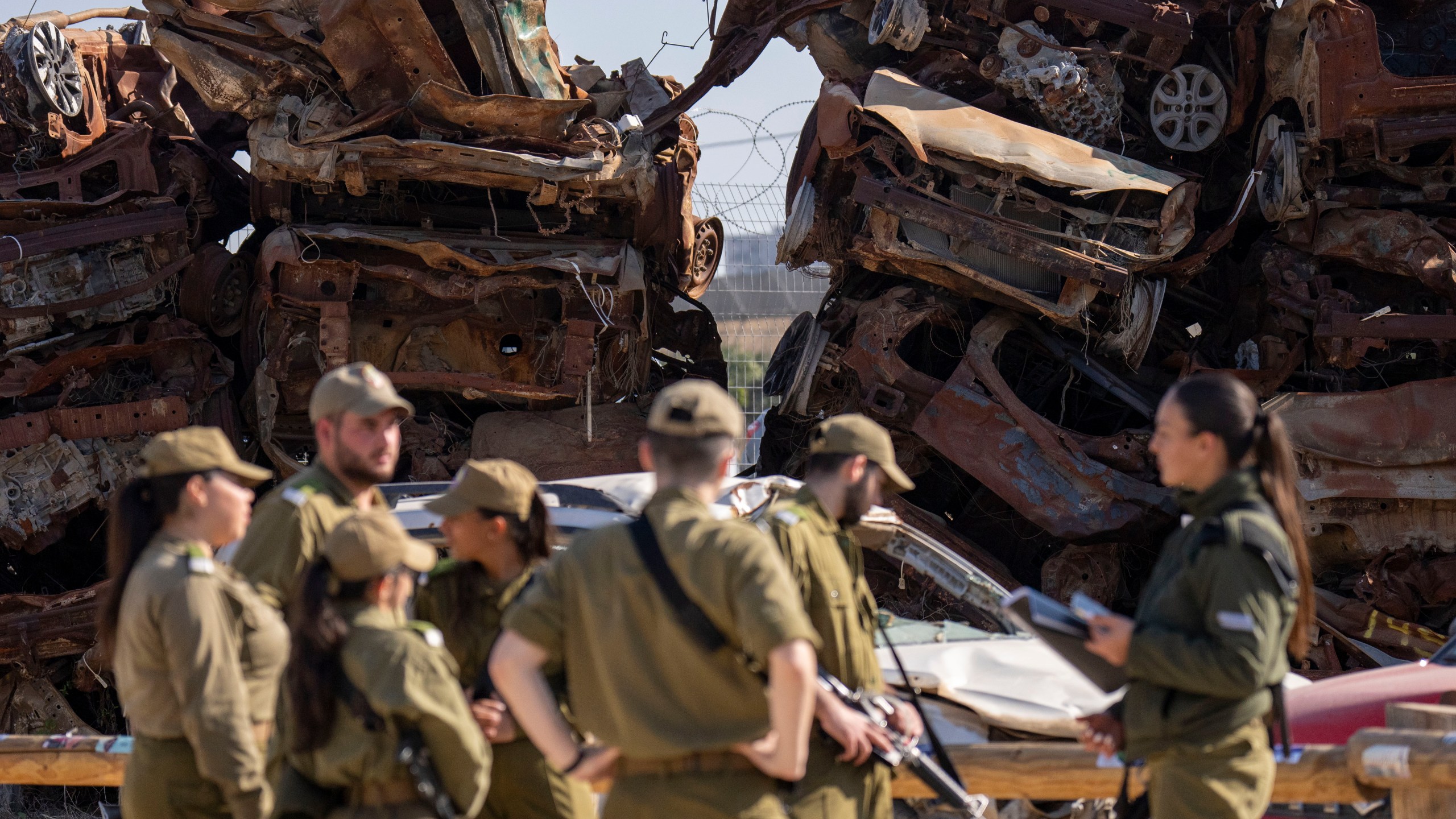 Israeli soldiers look at charred vehicles burned in the Oct. 7 , 2023, cross-border attacks by Hamas militants outside the town of Netivot, southern Israel, Monday, Jan. 13, 2025. (AP Photo/Ariel Schalit)