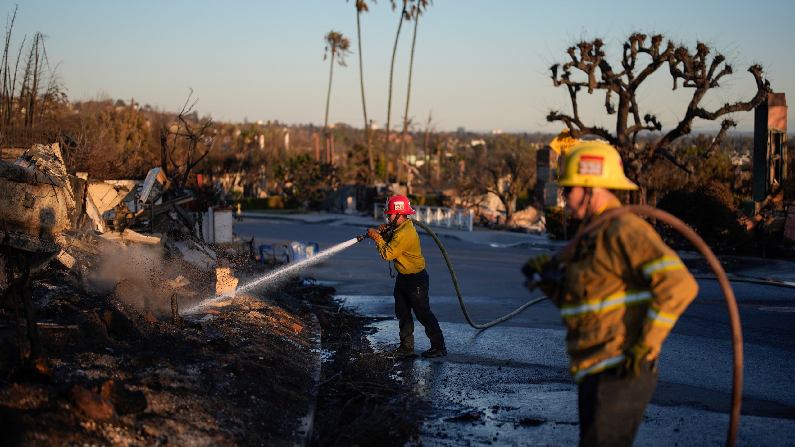 Apple Valley Fire District Captain Manuel Lafarga, center, and firefighter James Lyons hose down hotspots in the aftermath of the Palisades Fire in the Pacific Palisades neighborhood of Los Angeles, Monday, Jan. 13, 2025. (AP Photo/John Locher)