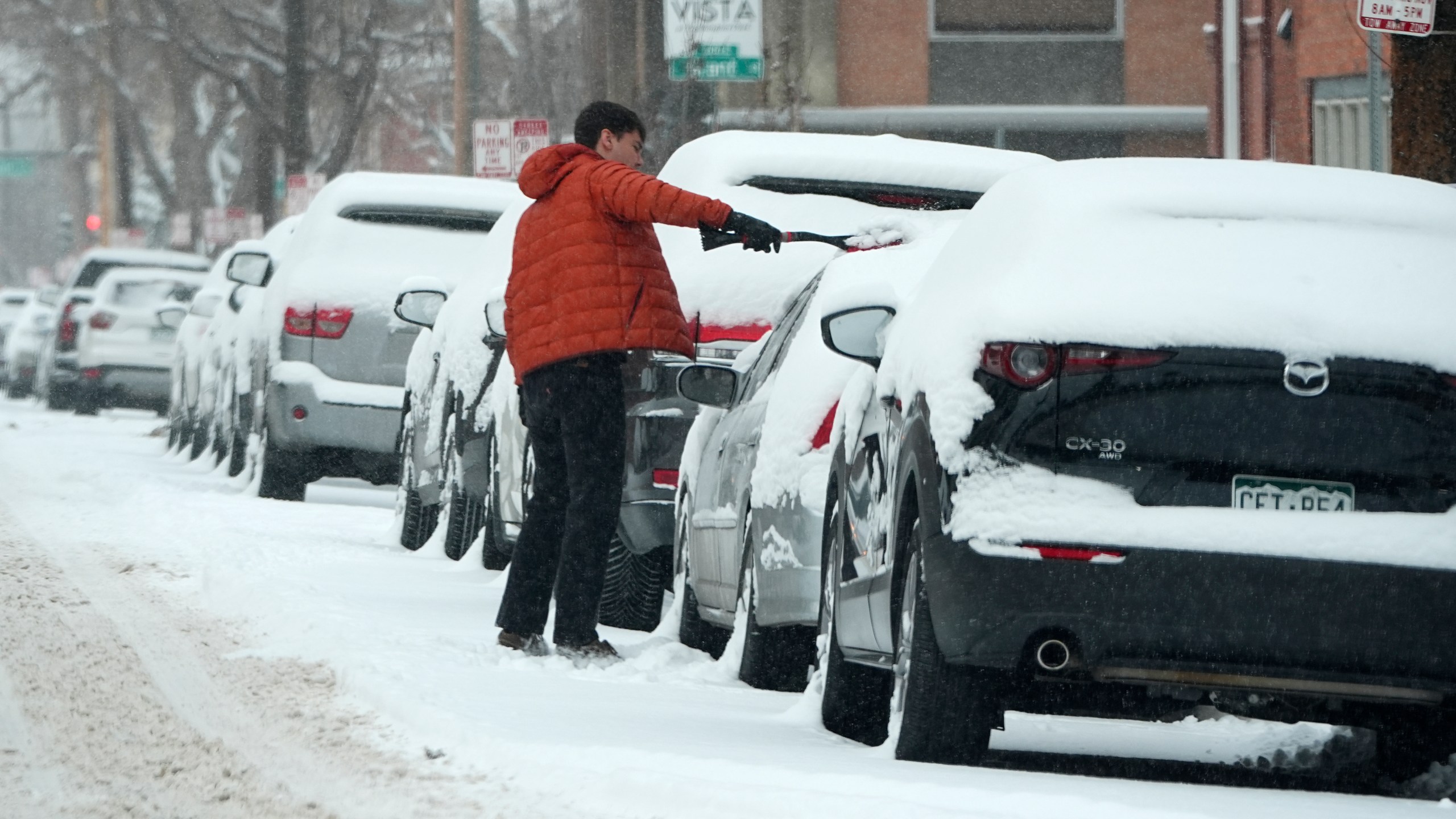 A motorist clears snow off his vehicle parked along First Avenue as a winter storm sweeps over the intermountain West, plunging temperatures into the single digits and bringing along a light snow in its wake Saturday, Jan. 18, 2025, in Denver. (AP Photo/David Zalubowski)