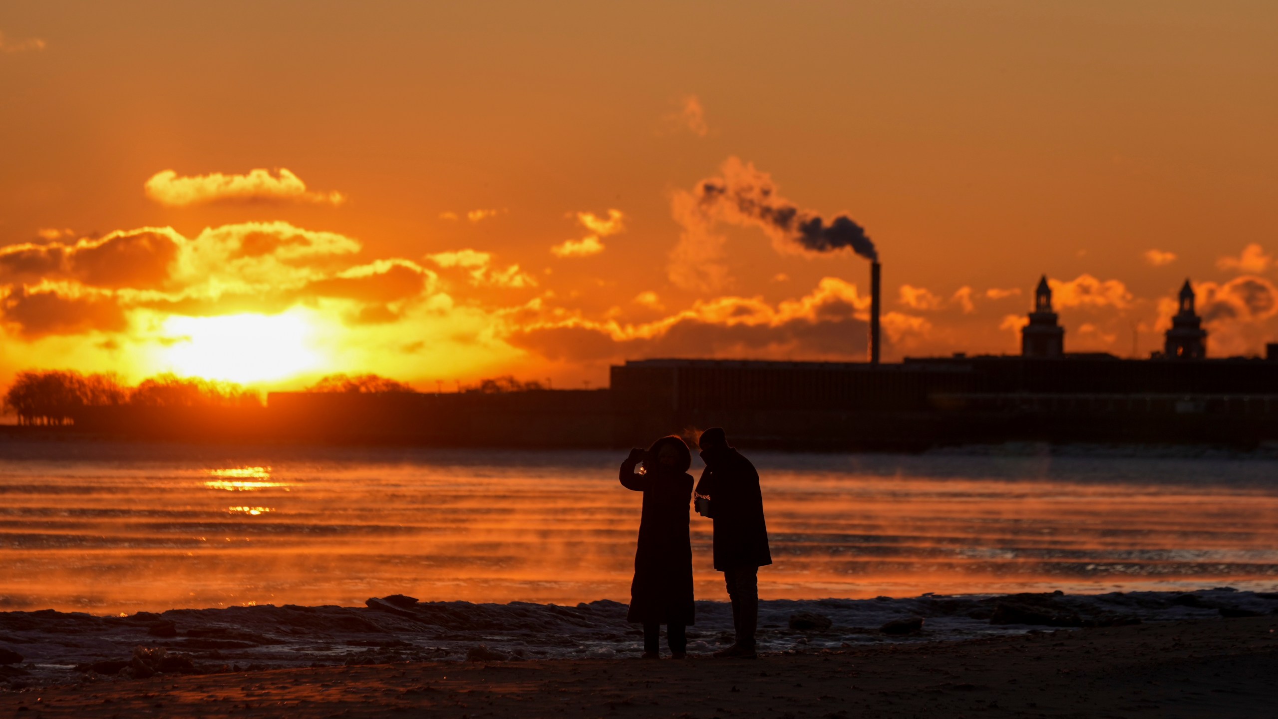 A couple take pictures at sunrise from the icy Oak Street Beach along the shore of Lake Michigan Monday, Jan. 20, 2025, in Chicago, as the weather service issued cold weather advisories across the Great Lakes region as high temperatures in many places were expected only to rise into the single digits Monday and Tuesday. (AP Photo/Kiichiro Sato)