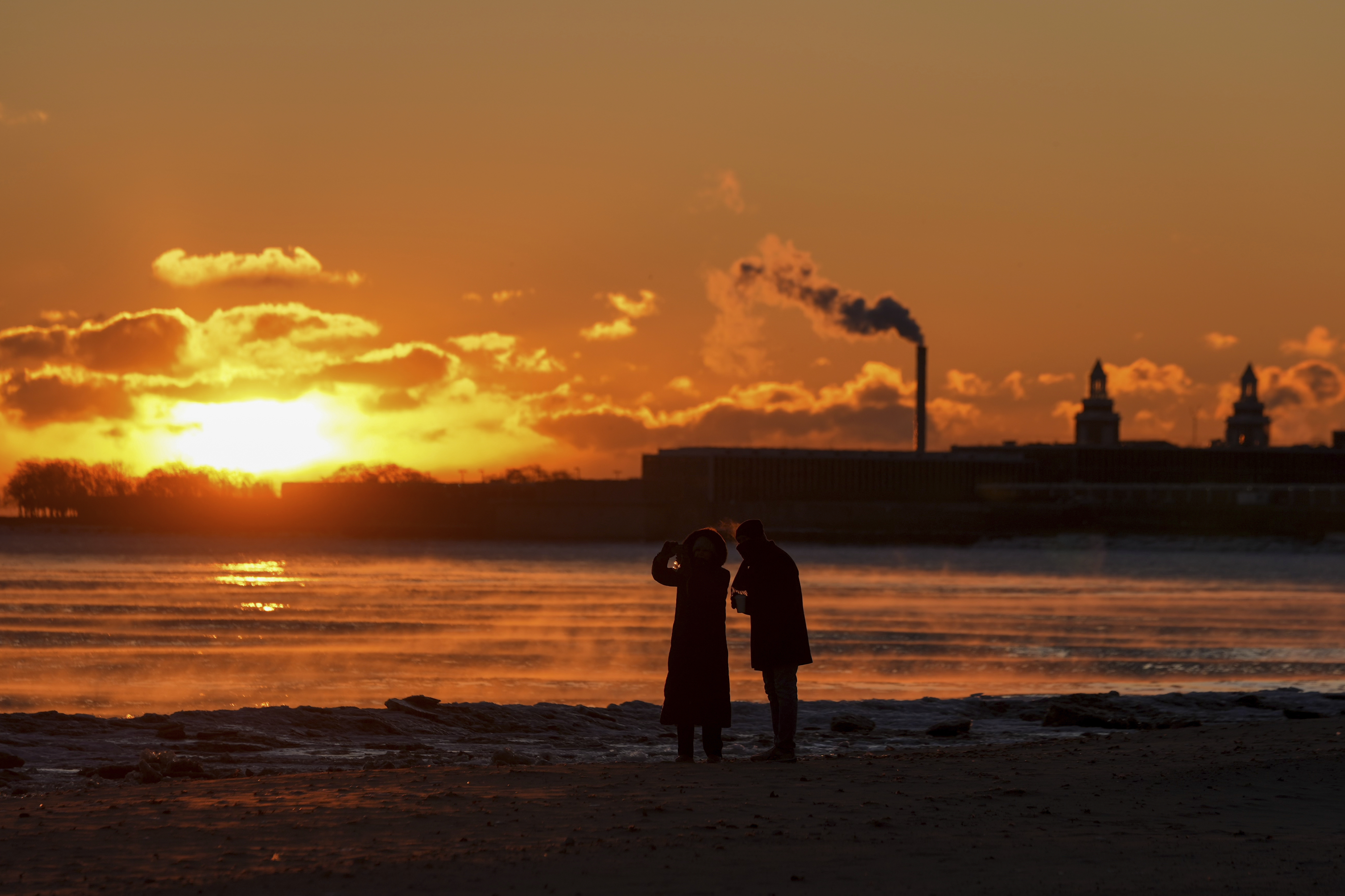 A couple take pictures at sunrise from the icy Oak Street Beach along the shore of Lake Michigan Monday, Jan. 20, 2025, in Chicago, as the weather service issued cold weather advisories across the Great Lakes region as high temperatures in many places were expected only to rise into the single digits Monday and Tuesday. (AP Photo/Kiichiro Sato)