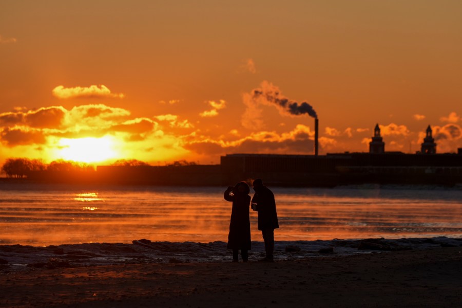 A couple take pictures at sunrise from the icy Oak Street Beach along the shore of Lake Michigan Monday, Jan. 20, 2025, in Chicago, as the weather service issued cold weather advisories across the Great Lakes region as high temperatures in many places were expected only to rise into the single digits Monday and Tuesday. (AP Photo/Kiichiro Sato)