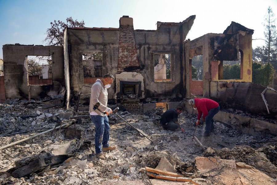 Homeowner David Marquez, left, holds a metal detector as his father, Juan Pablo Alvarado, right, and a friend look for the remains of gold jewelry and other silver items inside the walls of their multi-generational home in the aftermath of the Eaton Fire, Sunday, Jan. 19, 2025, in Altadena, Calif. (AP Photo/Damian Dovarganes)