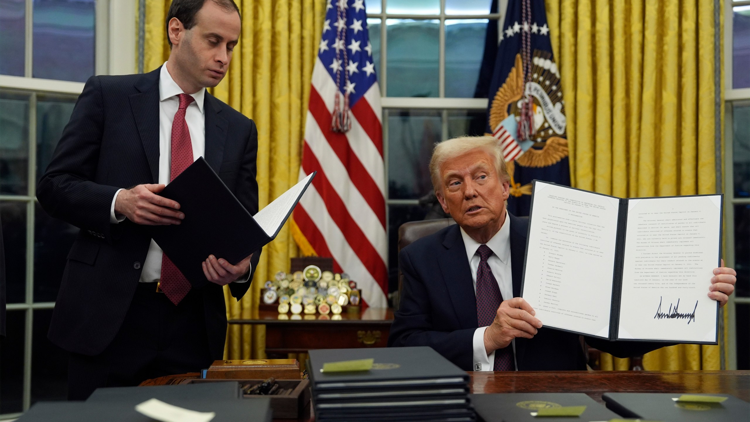 President Donald Trump holds up an executive order commuting sentences for people convicted of Jan. 6 offenses in the Oval Office of the White House, Monday, Jan. 20, 2025, in Washington. (AP Photo/Evan Vucci)