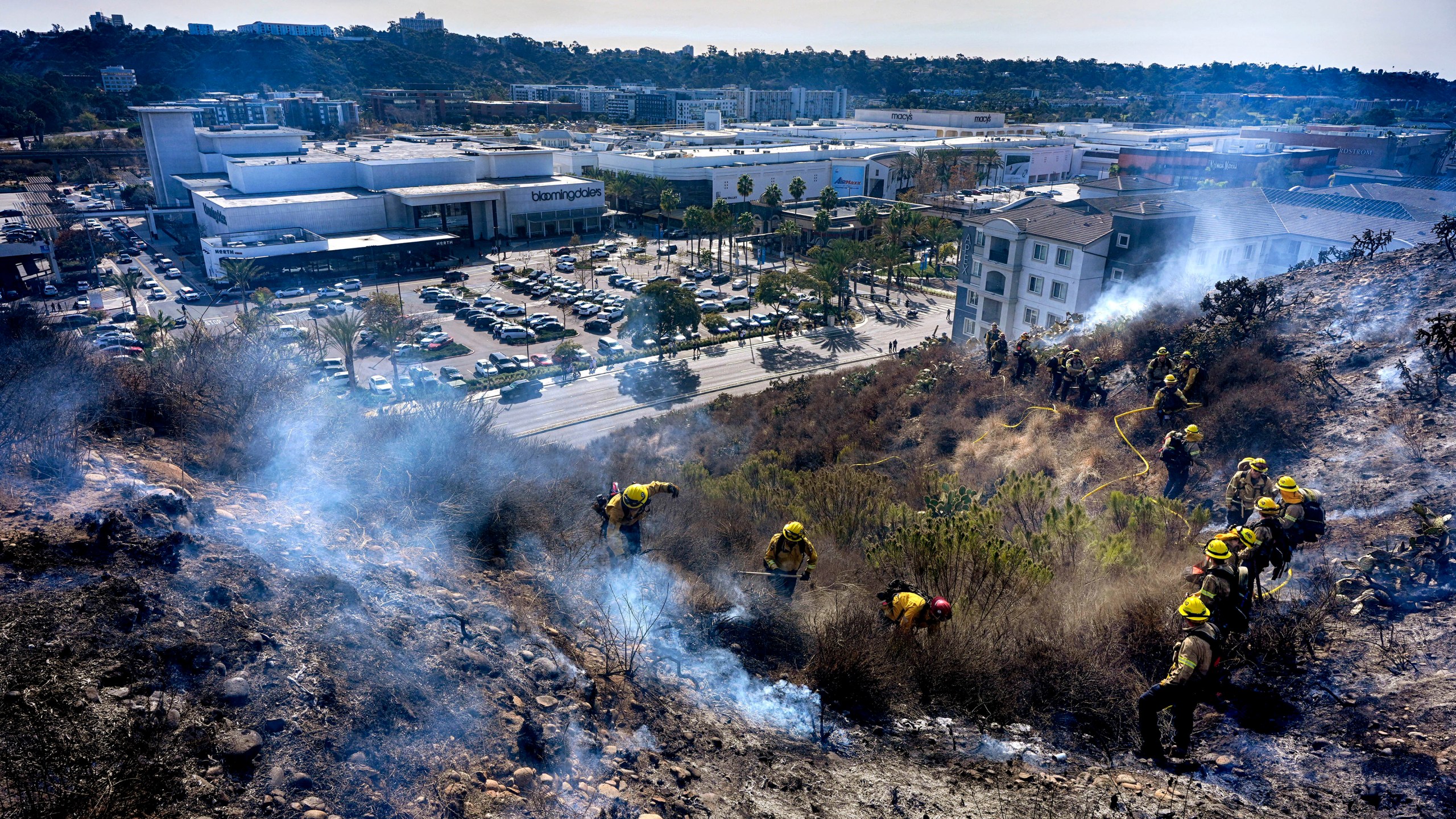 San Diego firefighters knock down a small brush along a hillside over the Mission Valley Shopping Mall in San Diego on Tuesday, Jan. 21, 2025. (AP Photo/Gregory Bull)