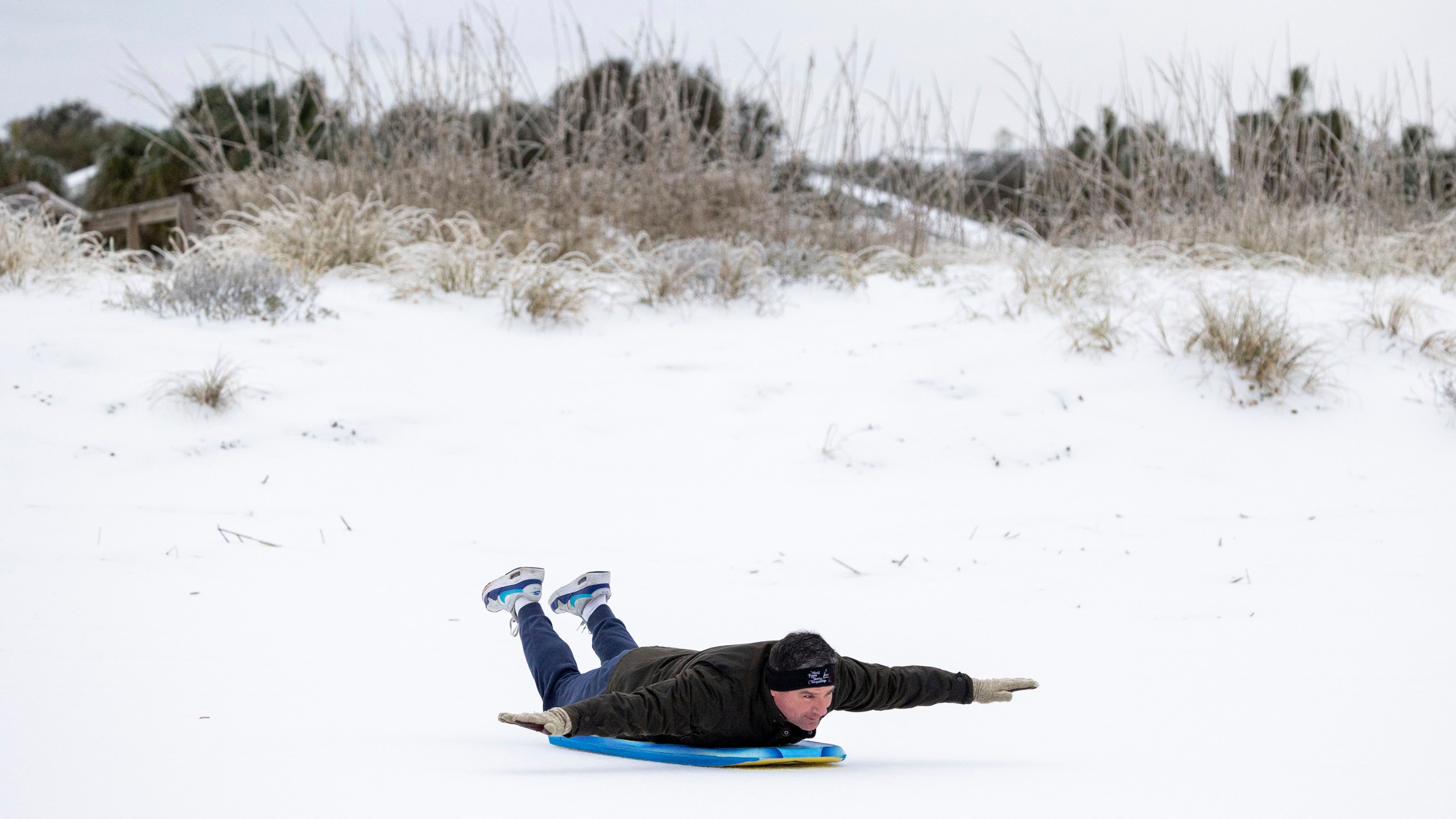 Alex Spiotta, from the Isle of Palms, S.C., uses a boogie board to sled across the beach after a winter storm dropped ice and snow Wednesday, Jan. 22, 2025, on the Isle of Palms, S.C. (AP Photo/Mic Smith)