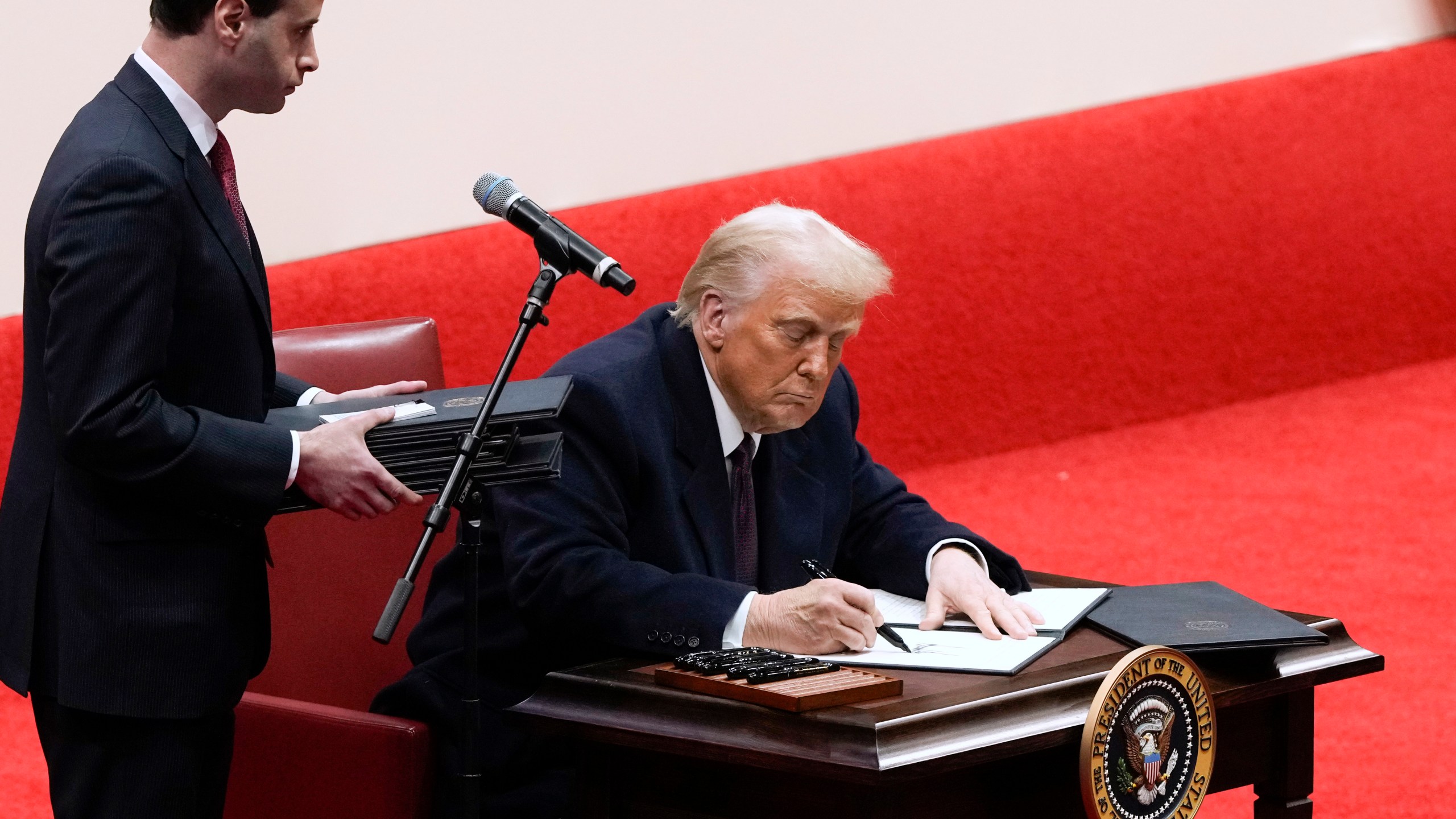 Will Scharf assists as President Donald Trump signs an executive order at an indoor Presidential Inauguration parade event in Washington, Monday, Jan. 20, 2025. (AP Photo/Susan Walsh)