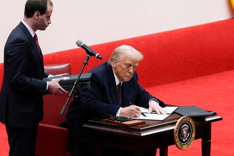 Will Scharf assists as President Donald Trump signs an executive order at an indoor Presidential Inauguration parade event in Washington, Monday, Jan. 20, 2025. (AP Photo/Susan Walsh)