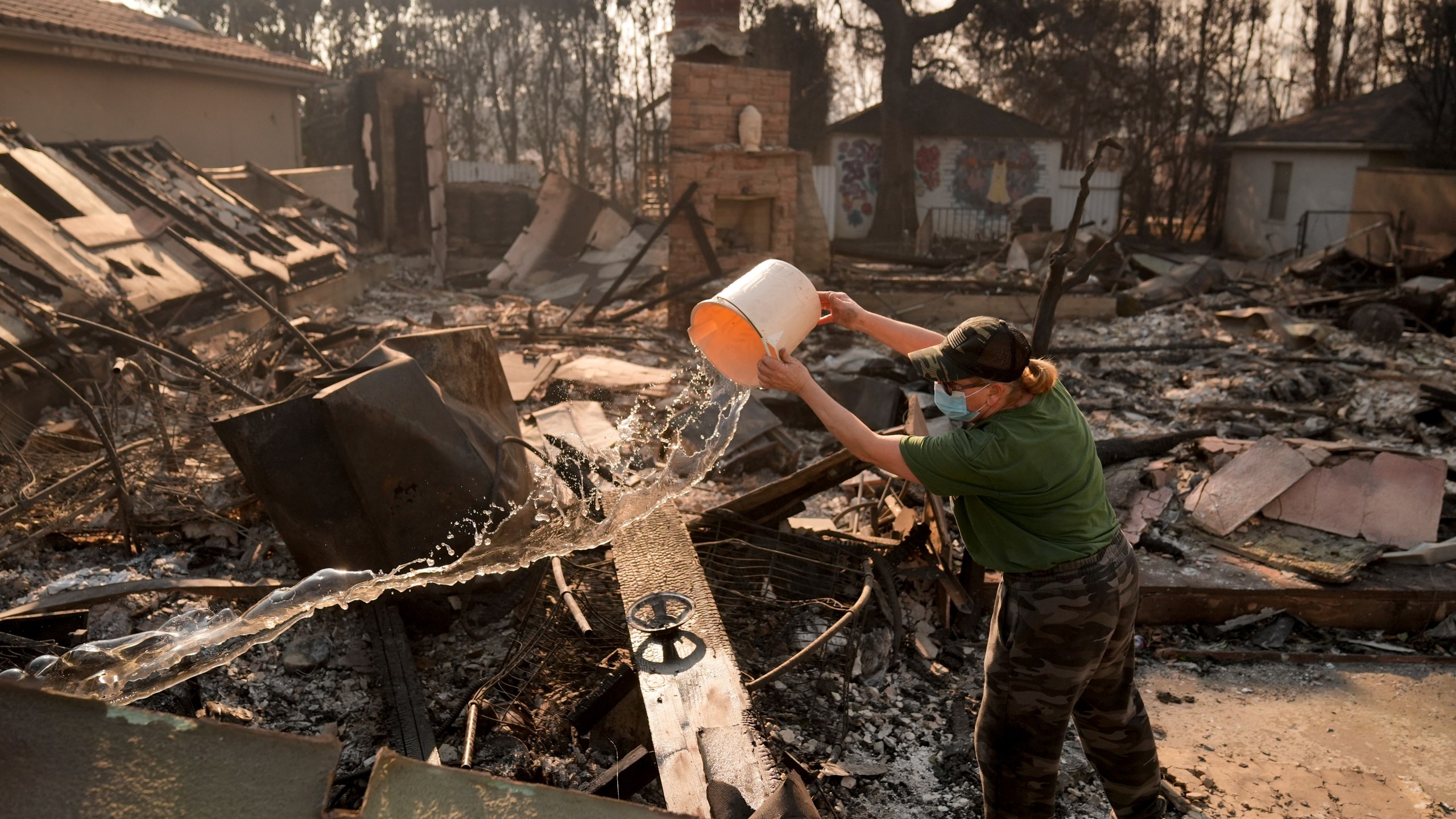 FILE - Nancy Belanger pours water on a neighbor's fire-ravaged property in the aftermath of the Palisades Fire in the Pacific Palisades neighborhood of Los Angeles, Thursday, Jan. 9, 2025. (AP Photo/Jae C. Hong,File)