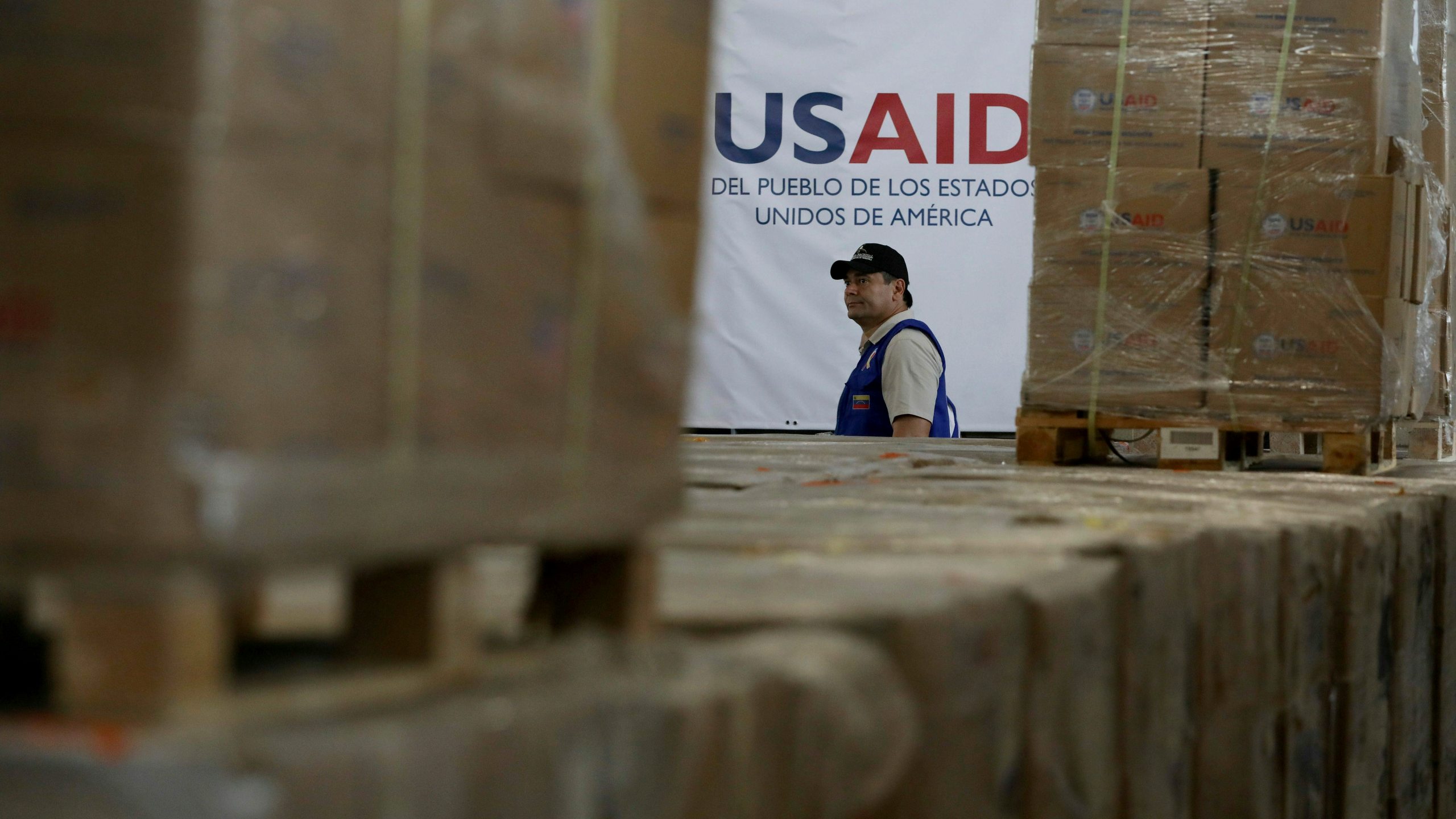 FILE - A man walks past boxes of USAID humanitarian aid at a warehouse at the Tienditas International Bridge on the outskirts of Cucuta, Colombia, Feb. 21, 2019, on the border with Venezuela. (AP Photo/Fernando Vergara)