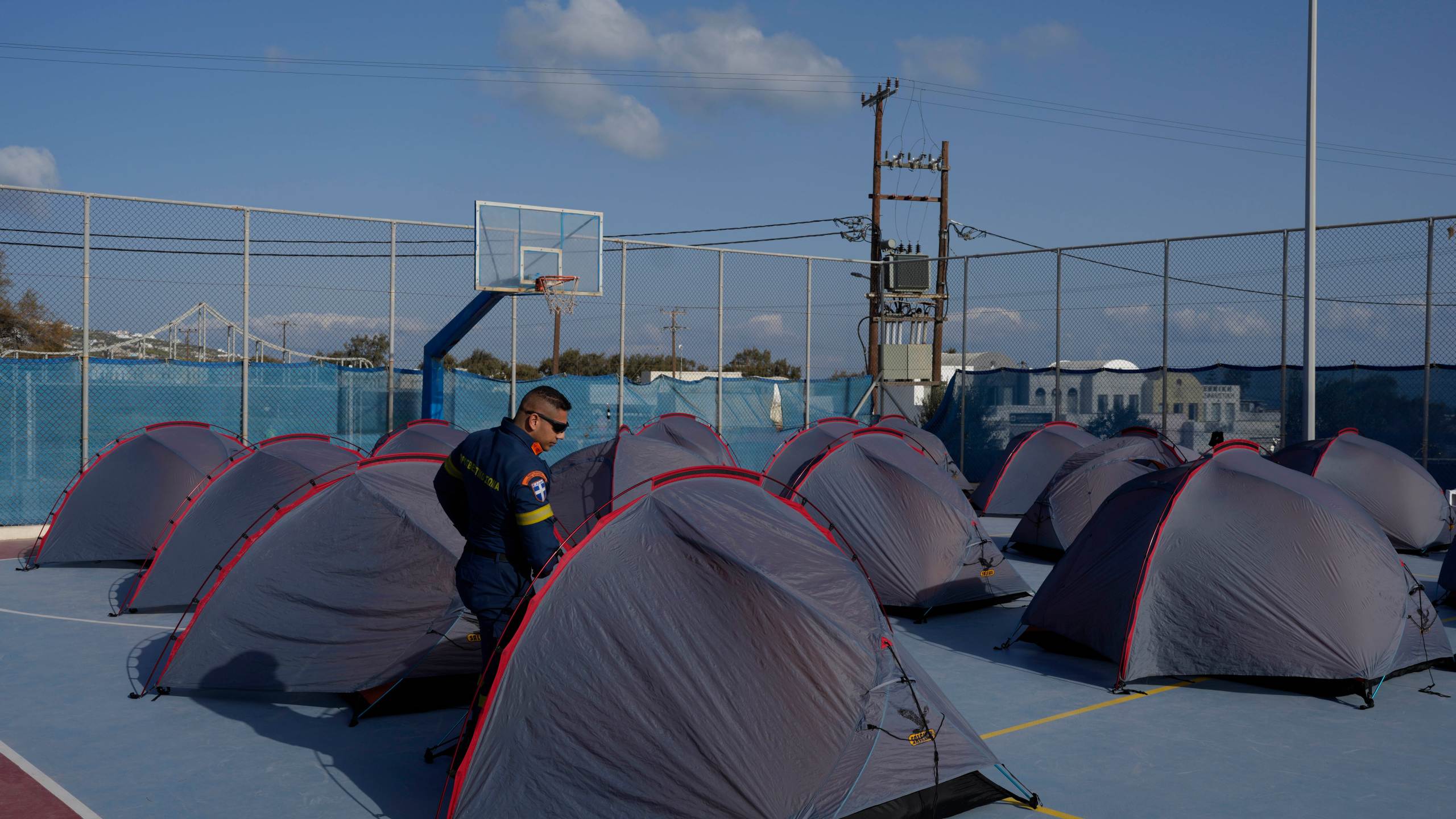 A firefighter walks among tents set up at a basketball court to accommodate Fire Service rescuers as Greek authorities are taking emergency measures in response to intense seismic activity on the popular Aegean Sea holiday island of Santorini, southern Greece, Monday, Feb. 3, 2025. (AP Photo/Petros Giannakouris)