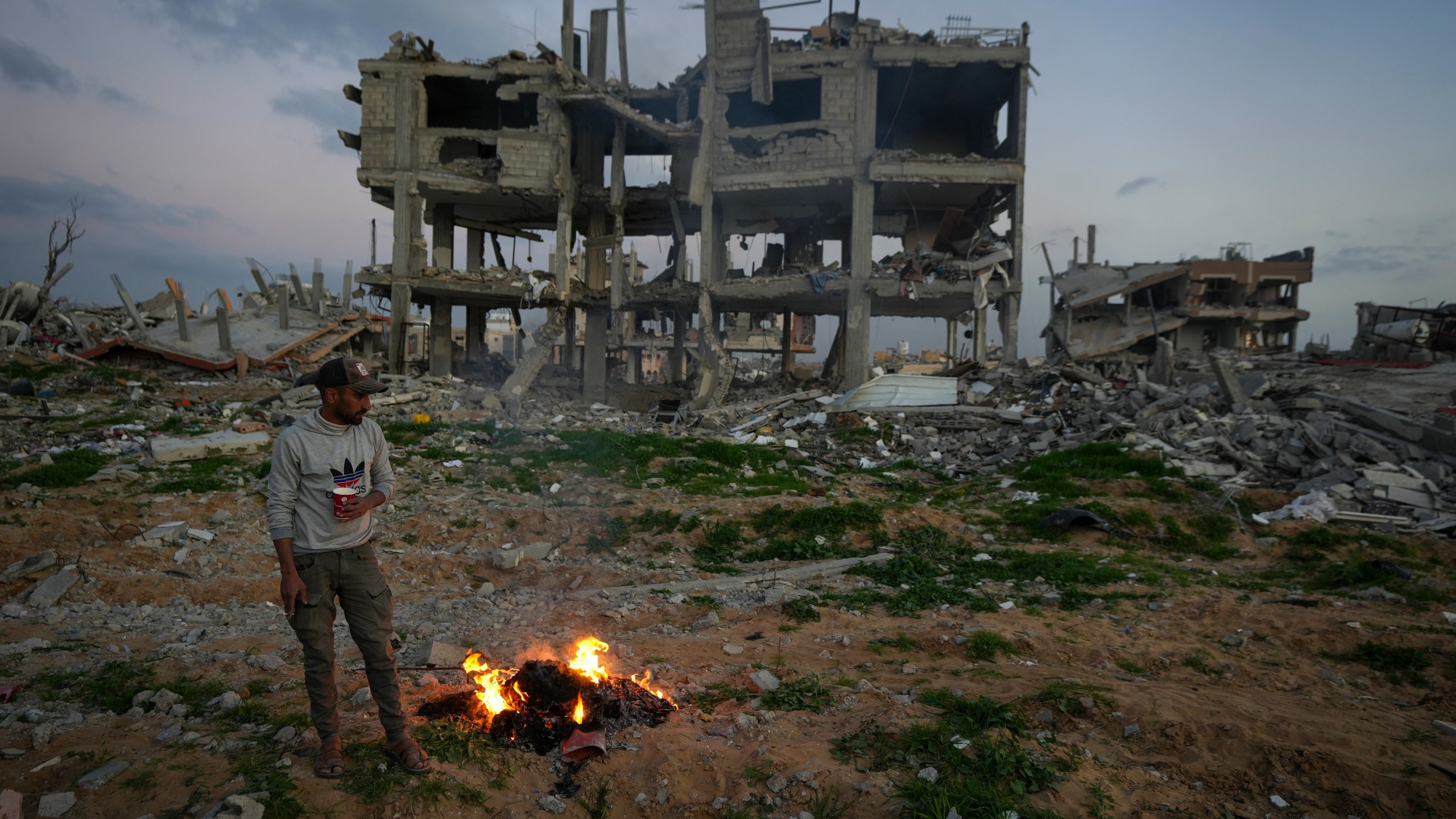 A man stands by a fire next to a destroyed house in an area littered with rubble from buildings demolished during the Israeli army's ground and air offensive against Hamas in Gaza City, Tuesday Feb. 4, 2025.(AP Photo/Abdel Kareem Hana)