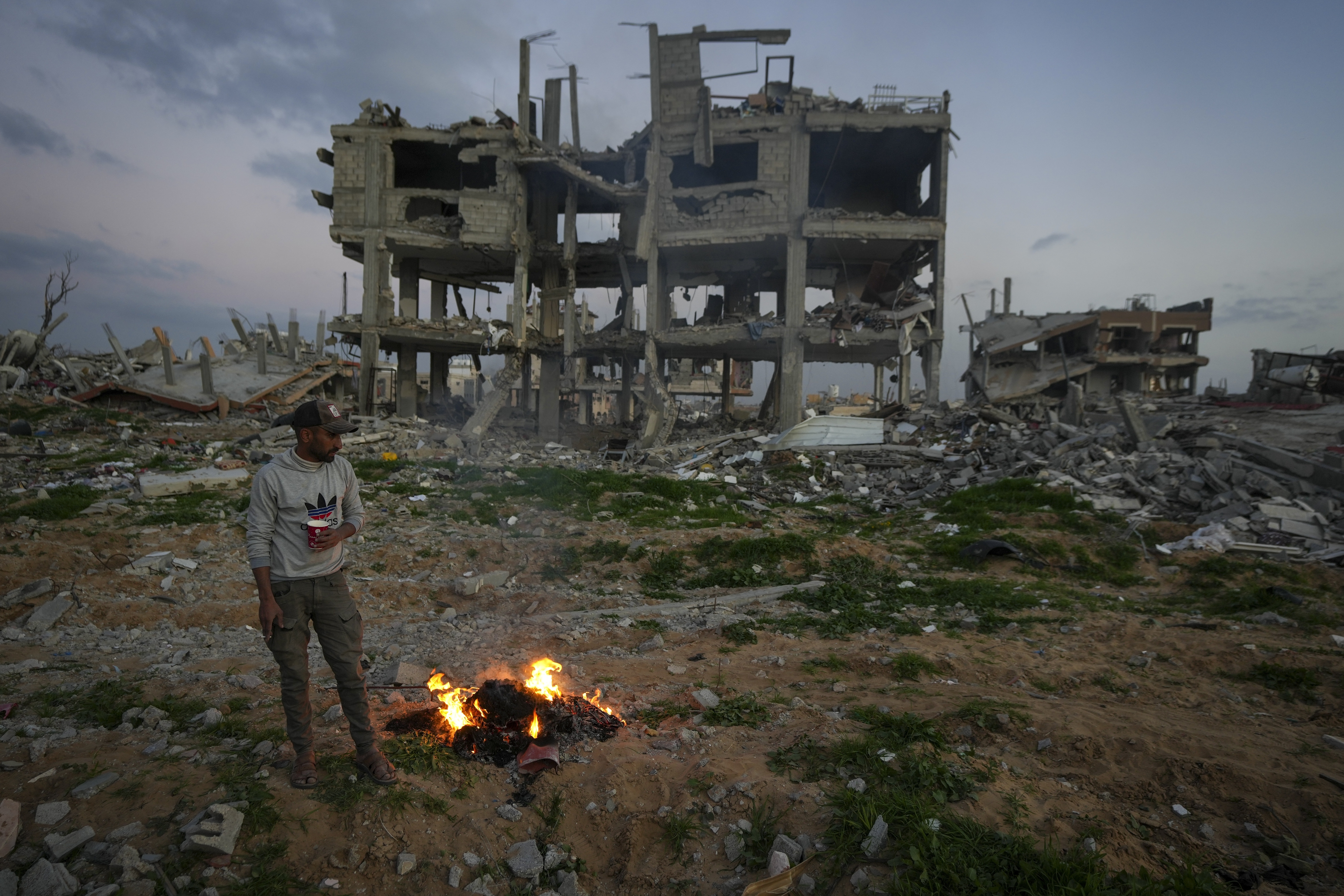 A man stands by a fire next to a destroyed house in an area littered with rubble from buildings demolished during the Israeli army's ground and air offensive against Hamas in Gaza City, Tuesday Feb. 4, 2025.(AP Photo/Abdel Kareem Hana)