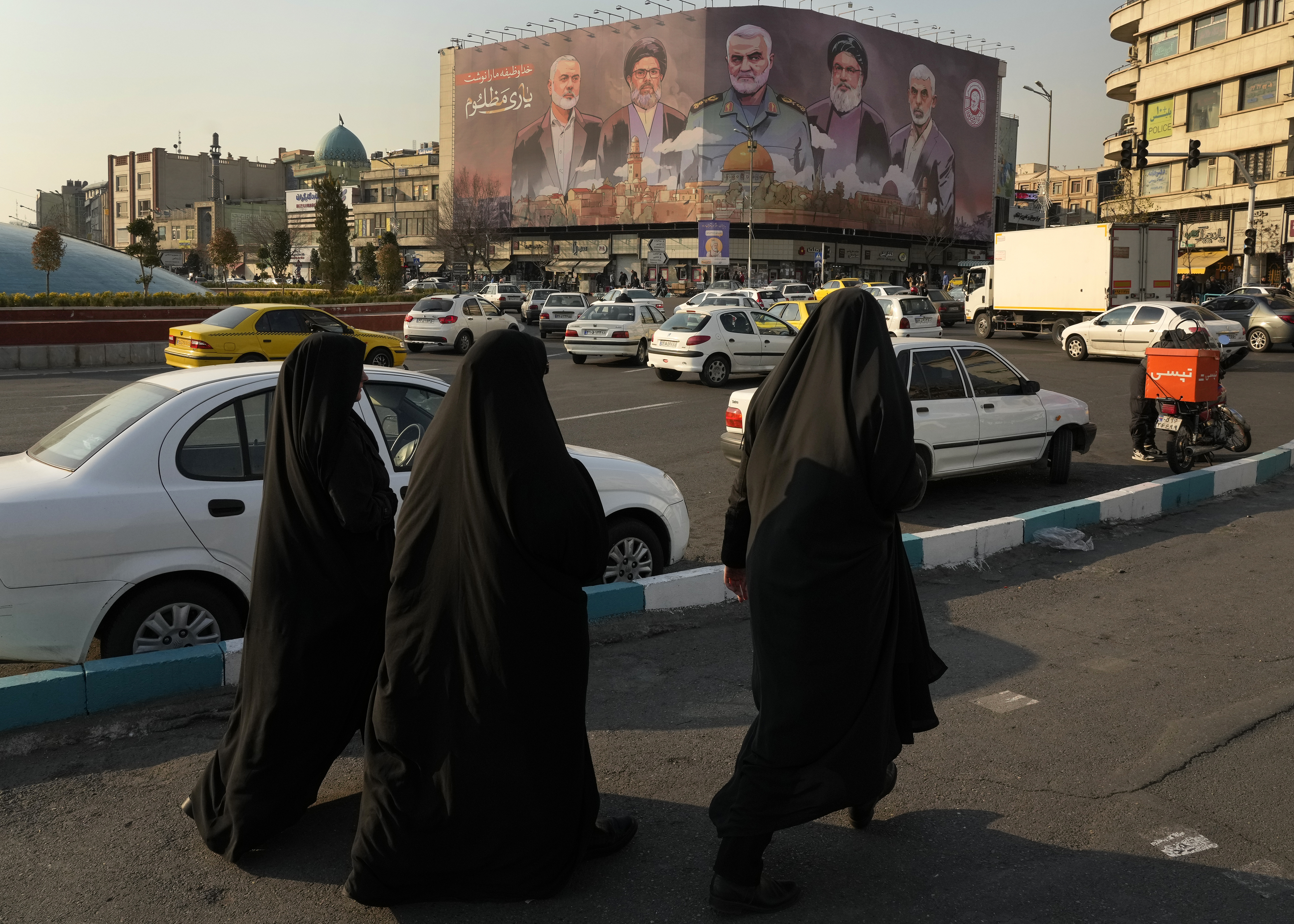 People walk on Enqelab-e-Eslami (Islamic Revolution) square near a huge banner showing the late commander of the Iran's Revolutionary Guard expeditionary Quds Force, Gen. Qassem Soleimani, center, who was killed in a U.S. drone attack in 2020, and Hezbollah and Hamas officials killed by Israel, in Tehran, Iran, Tuesday, Jan. 21, 2025. (AP Photo/Vahid Salemi)