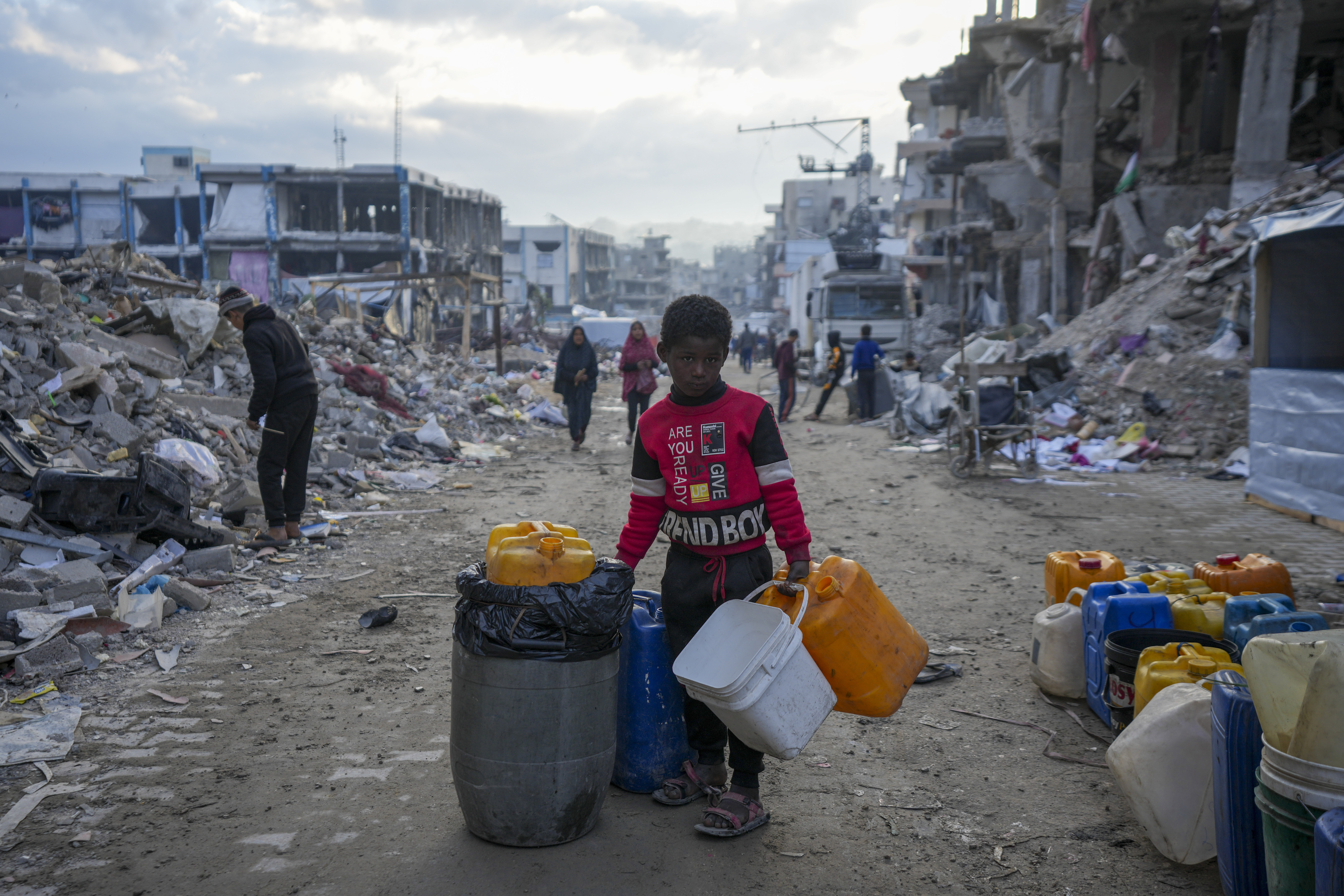 A young Palestinian kid carries jerricans along the destruction caused by the Israeli air and ground offensive in Jabaliya, Gaza Strip, Wednesday, Feb. 5, 2025. (AP Photo/Abdel Kareem Hana)