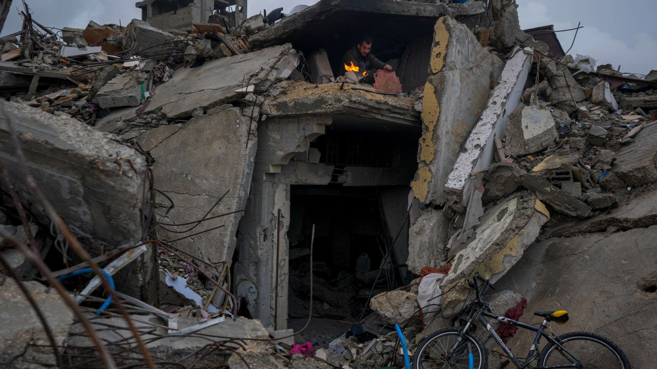 Mohammad Naser, sits by a fire as he takes cover from the rain under the destruction of his house caused by the Israeli air and ground offensive in Jabaliya, Gaza Strip, Thursday, Feb. 6, 2025. (AP Photo/Abdel Kareem Hana)