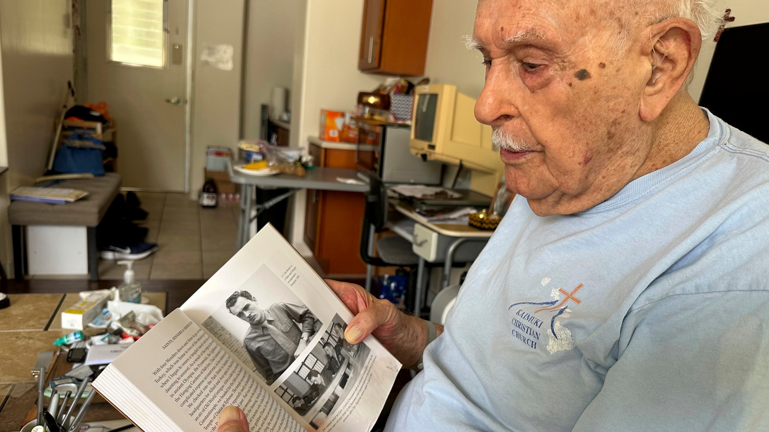 Jim Becker, a former Associated Press journalist, holds a book showing a 1945 photo of him as a Stars and Stripes correspondent in Shanghai, at his home in Kaneohe, Hawaii, May 21, 2024. (AP Photo/Audrey McAvoy)