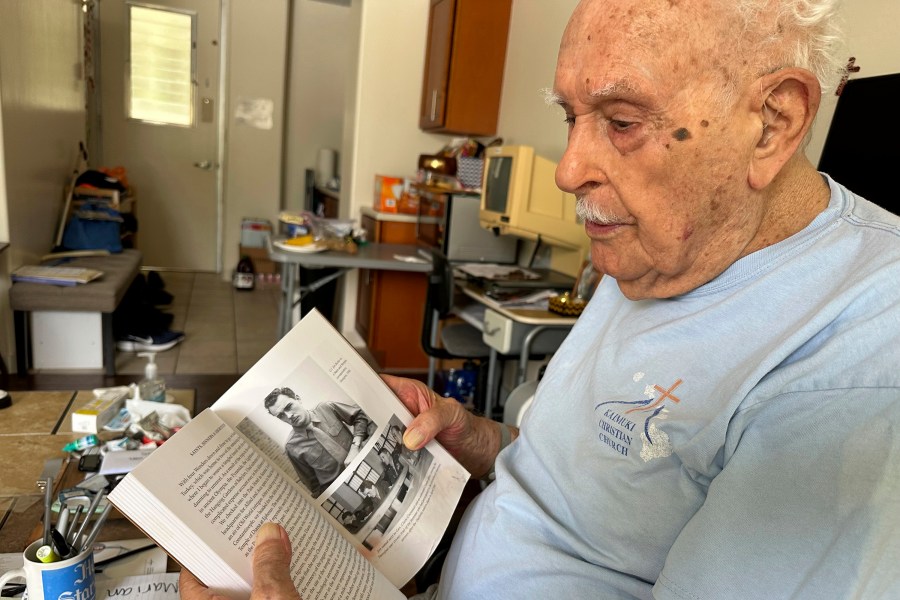 Jim Becker, a former Associated Press journalist, holds a book showing a 1945 photo of him as a Stars and Stripes correspondent in Shanghai, at his home in Kaneohe, Hawaii, May 21, 2024. (AP Photo/Audrey McAvoy)