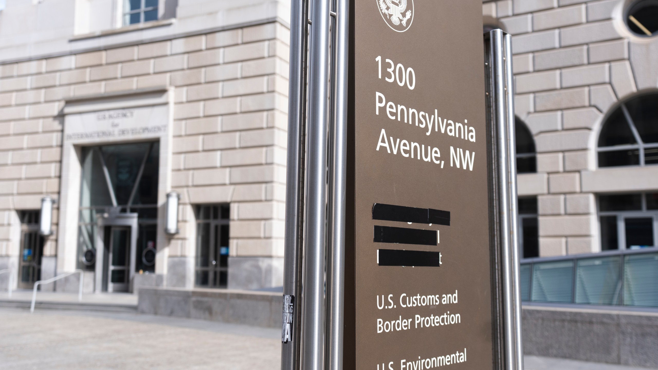 A street sign with names of U.S. government agencies housed at the Ronald Reagan Building, including the United States Agency for International Development, or USAID headquarters in Washington, is pictured with one building occupant taped, Friday, Feb. 7, 2025, in Washington. (AP Photo/Manuel Balce Ceneta)