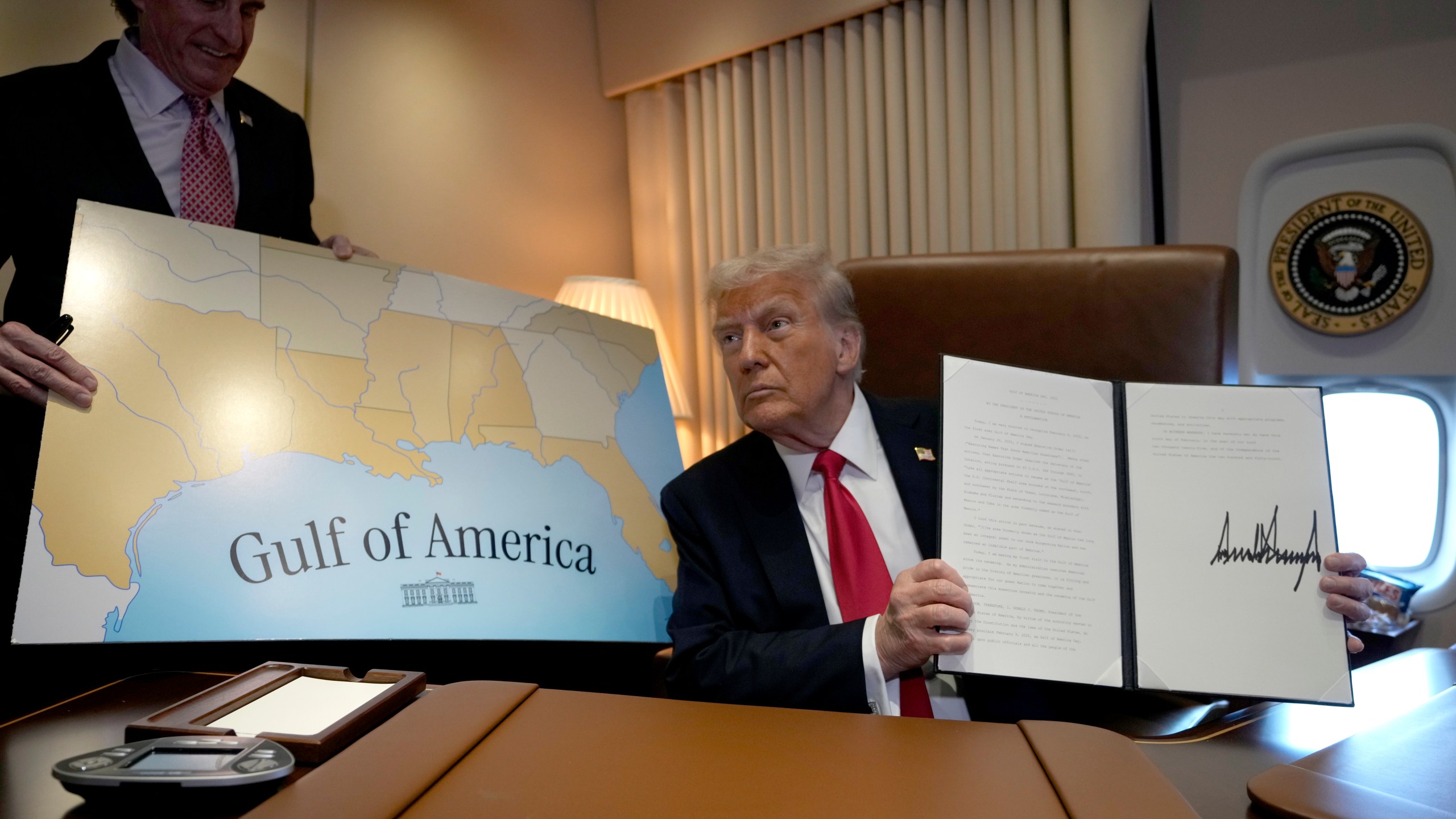 President Donald Trump holds up a signed proclamation declaring Feb. 9 Gulf of America Day, as Interior Secretary Doug Burgum watches aboard Air Force One as Trump travels from West Palm Beach, Fla. to New Orleans, Sunday, Feb. 9, 2025. (AP Photo/Ben Curtis)