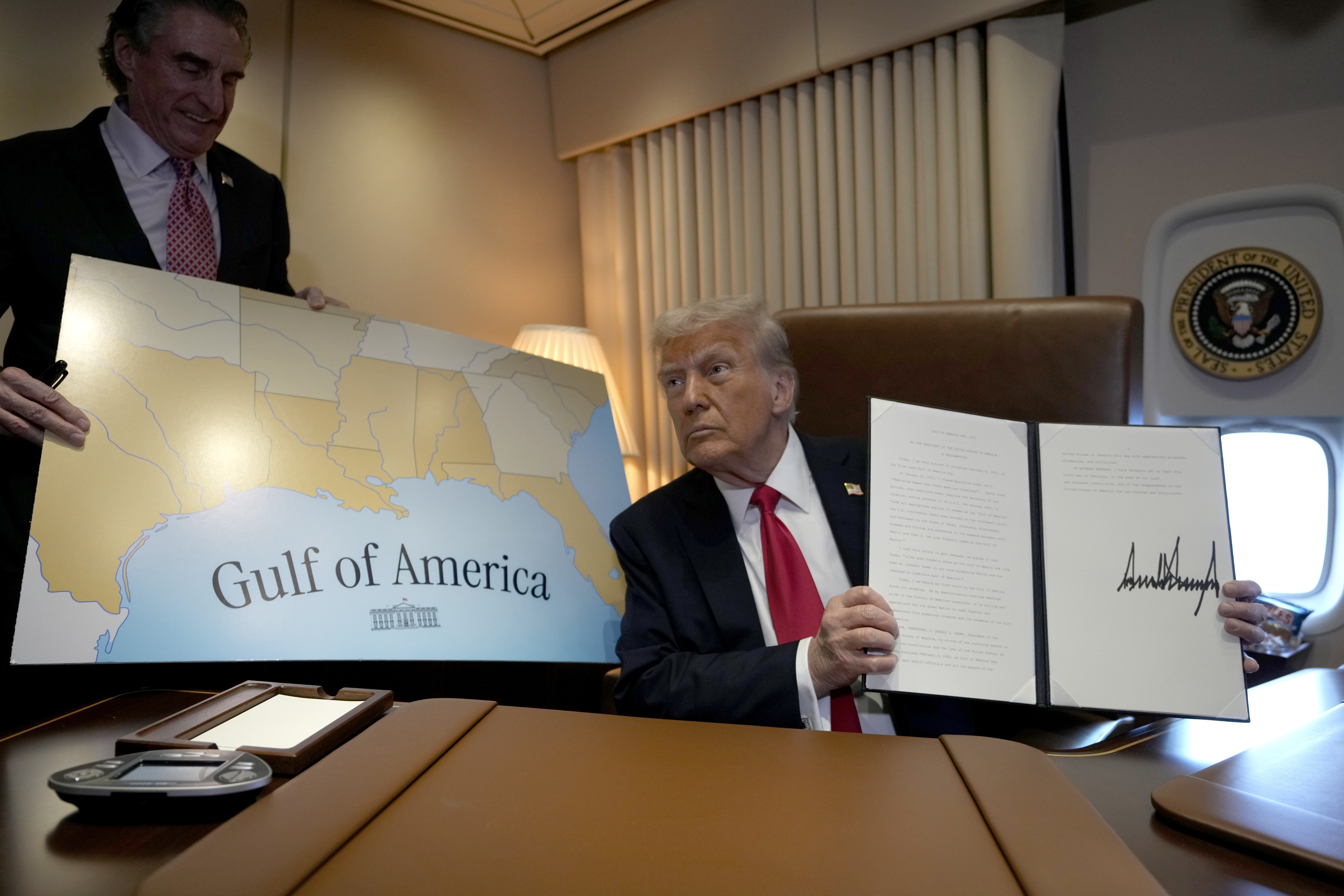 President Donald Trump holds up a signed proclamation declaring Feb. 9 Gulf of America Day, as Interior Secretary Doug Burgum watches aboard Air Force One as Trump travels from West Palm Beach, Fla. to New Orleans, Sunday, Feb. 9, 2025. (AP Photo/Ben Curtis)