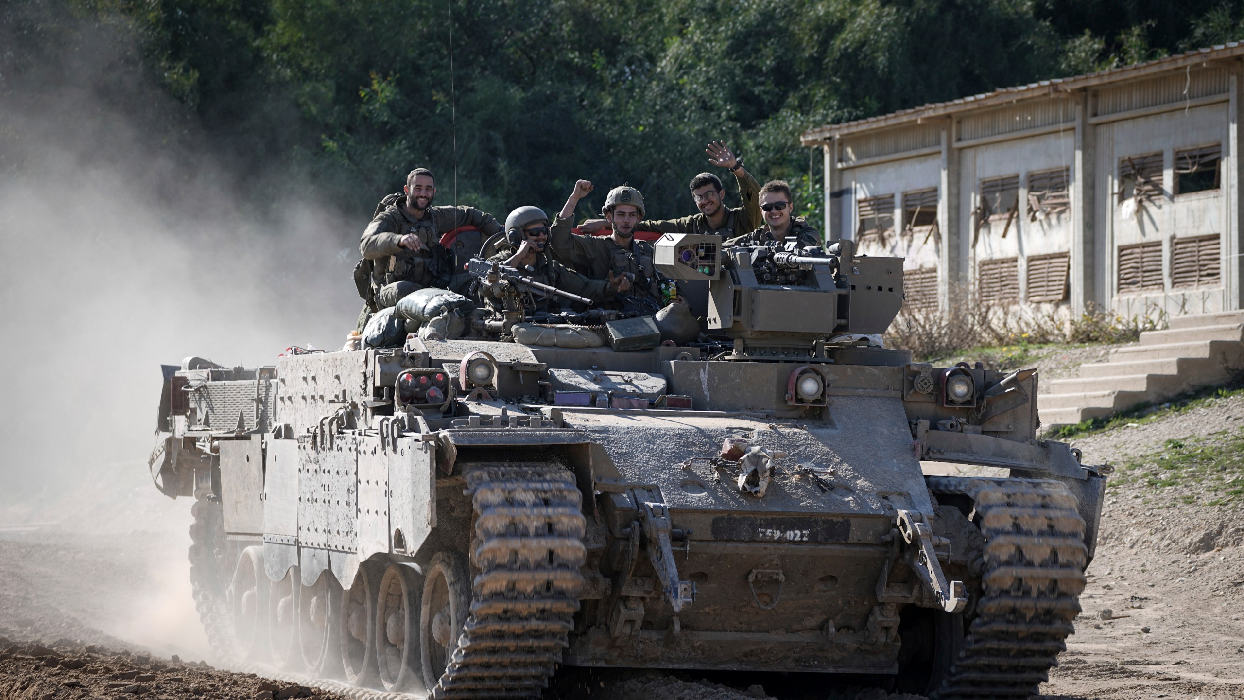 Israeli soldiers wave to the camera from an APC as they cross from the Gaza Strip into Israel, Saturday, Jan. 18, 2025. (AP Photo/Tsafrir Abayov)