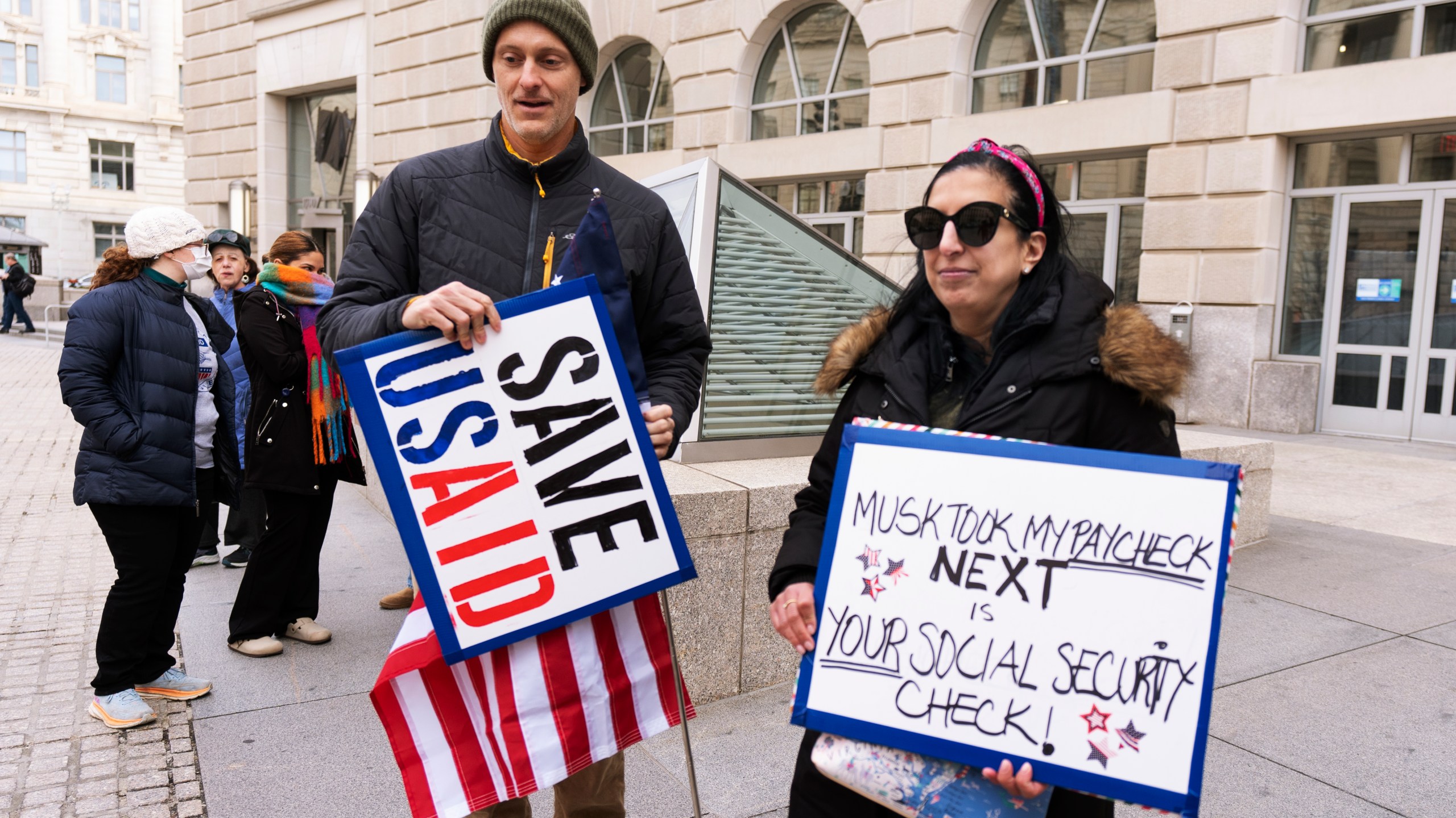 Priya Kathpal, right, and Taylor Williamson, left, who work for a company doing contract work for the United States Agency for International Development, or USAID, carry signs outside the USAID headquarters in Washington, Monday, Feb. 10, 2025. (AP Photo/Manuel Balce Ceneta)