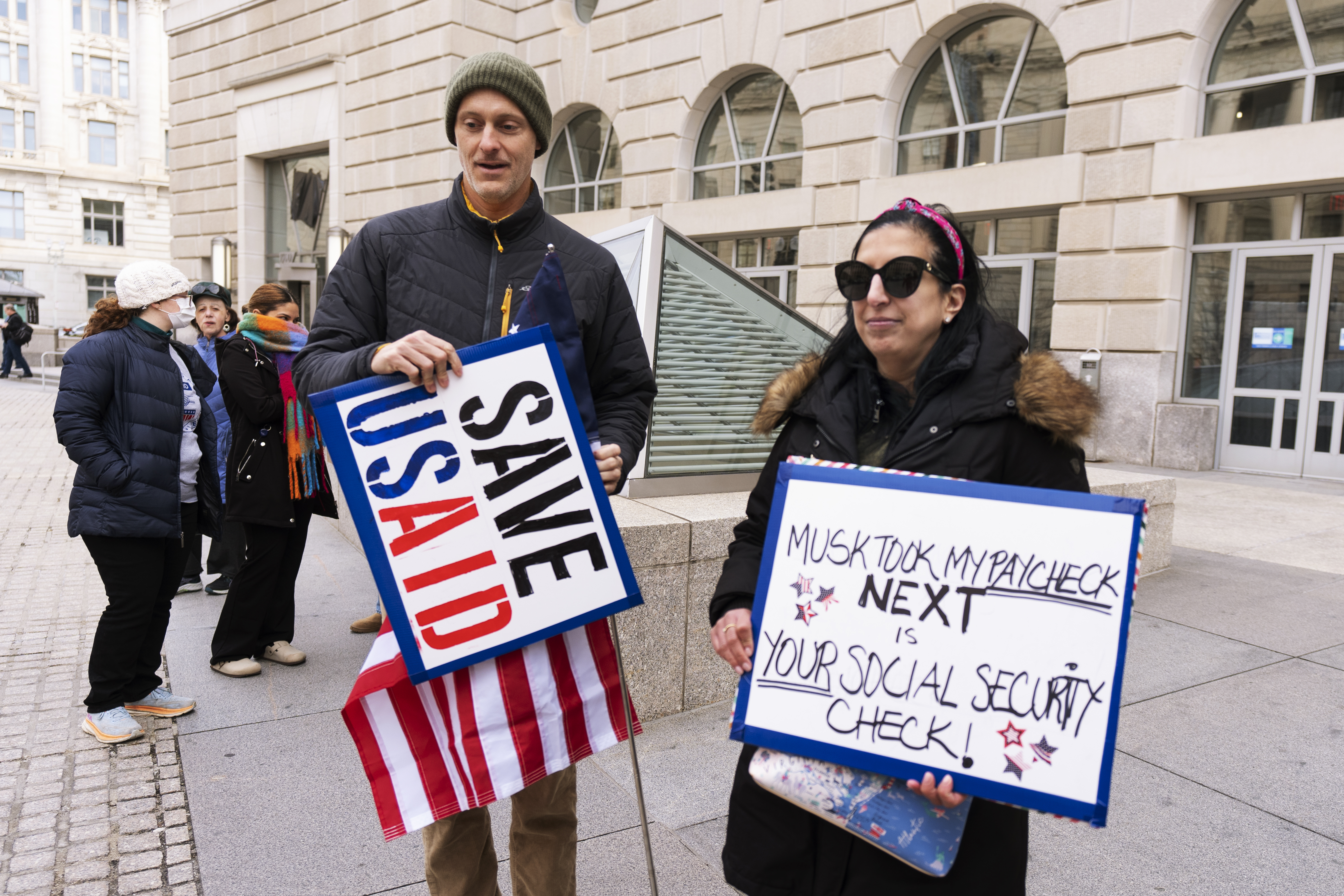 Priya Kathpal, right, and Taylor Williamson, left, who work for a company doing contract work for the United States Agency for International Development, or USAID, carry signs outside the USAID headquarters in Washington, Monday, Feb. 10, 2025. (AP Photo/Manuel Balce Ceneta)