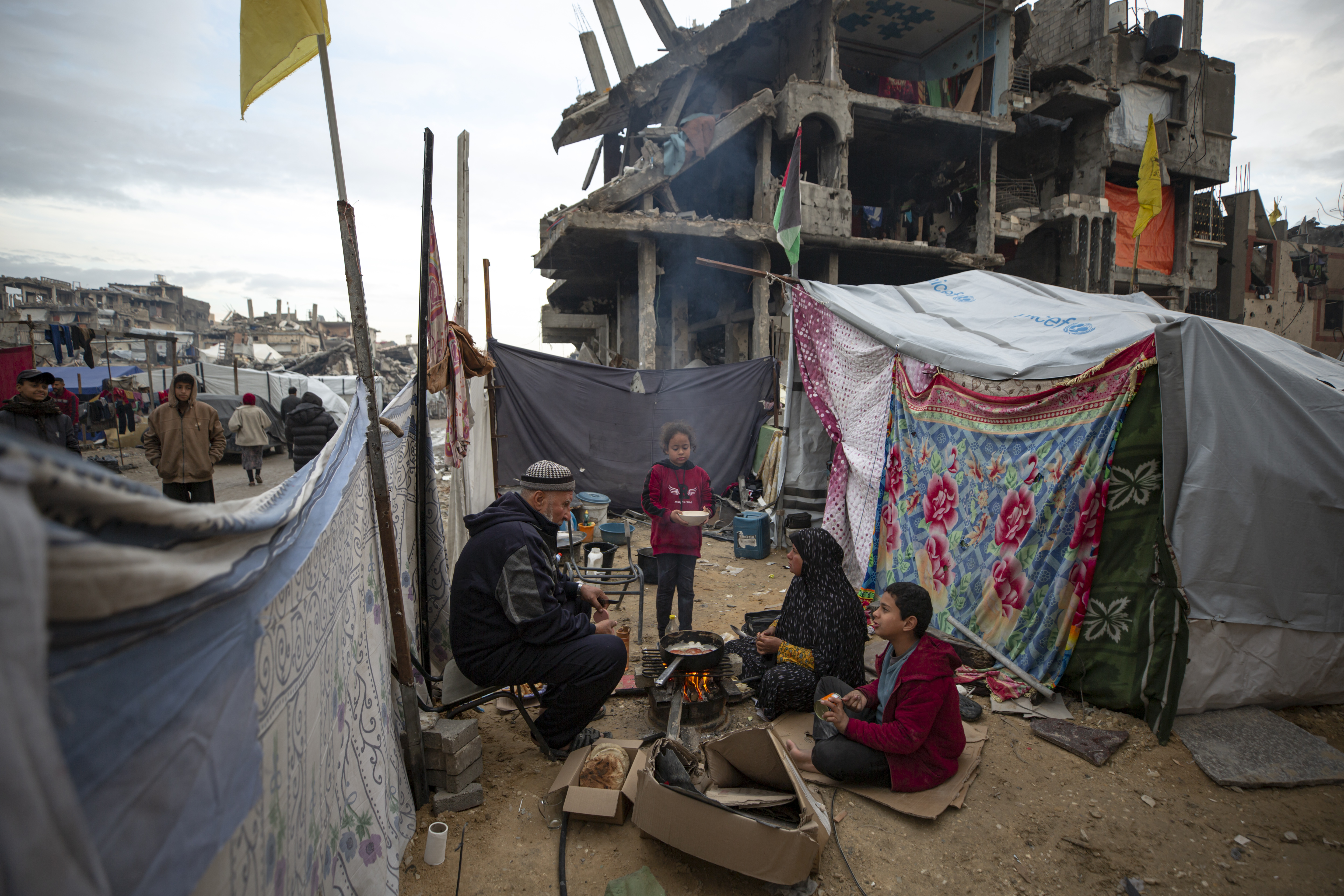 A Palestinian family cooks on fire next to their tent, in an area largely destroyed by the Israeli army's air and ground offensive in Jabaliya, Gaza Strip, on Tuesday, Feb. 11, 2025. (AP Photo/Jehad Alshrafi)