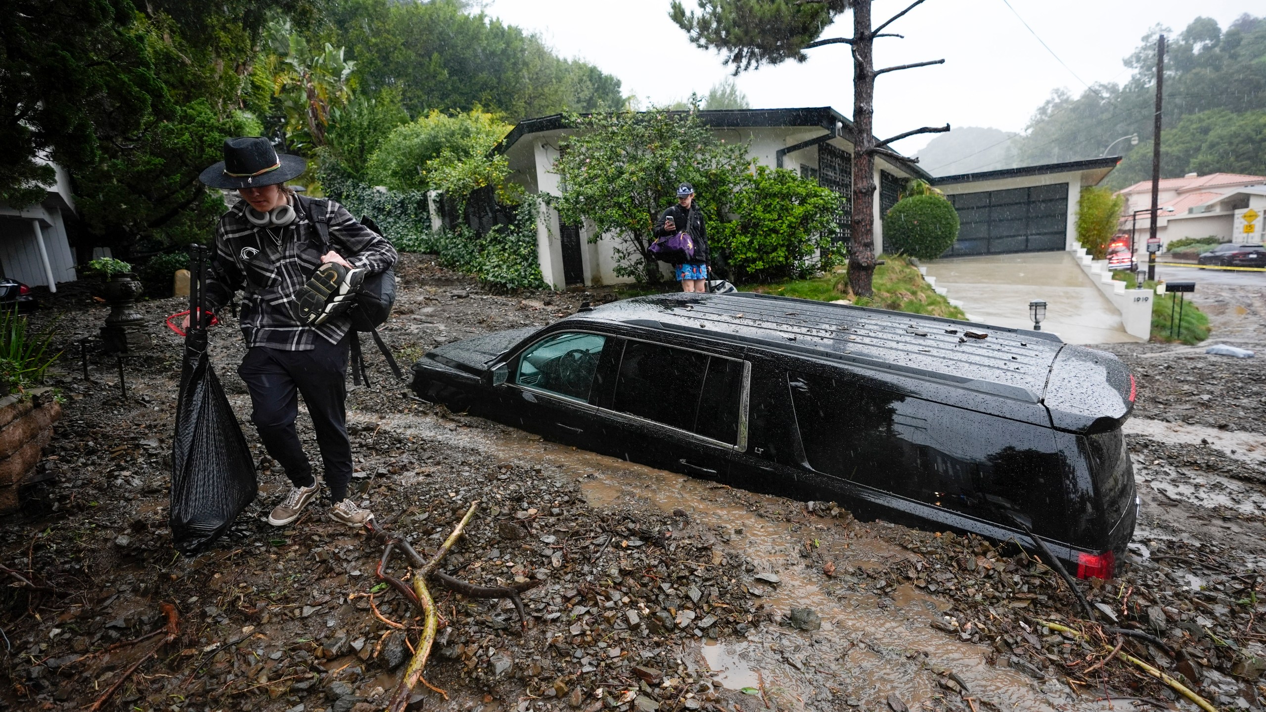 FILE - Residents evacuate past damaged vehicles after storms caused a mudslide, Monday, Feb. 5, 2024, in the Beverly Crest area of Los Angeles. (AP Photo/Marcio Jose Sanchez, File)