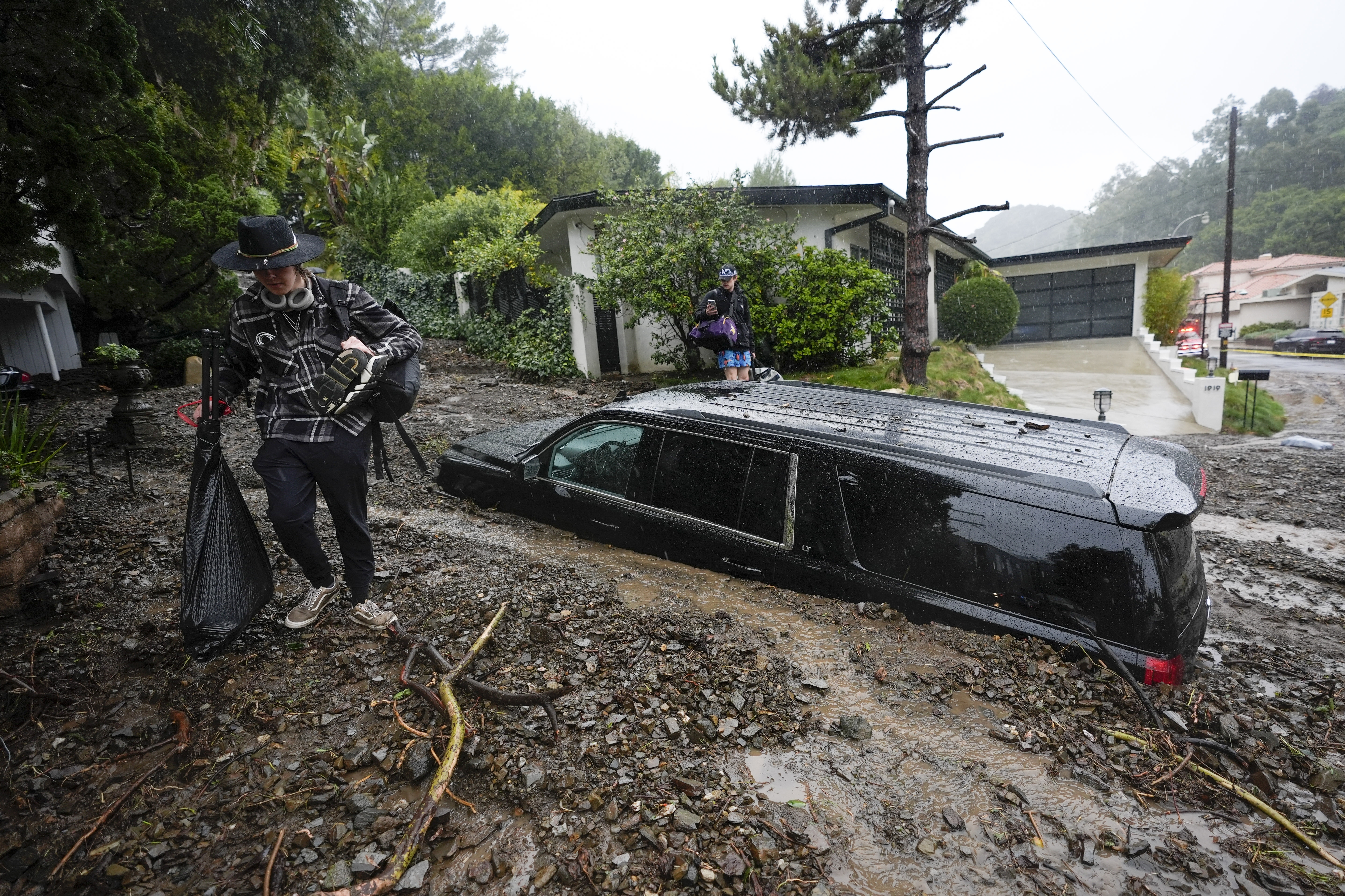 FILE - Residents evacuate past damaged vehicles after storms caused a mudslide, Monday, Feb. 5, 2024, in the Beverly Crest area of Los Angeles. (AP Photo/Marcio Jose Sanchez, File)