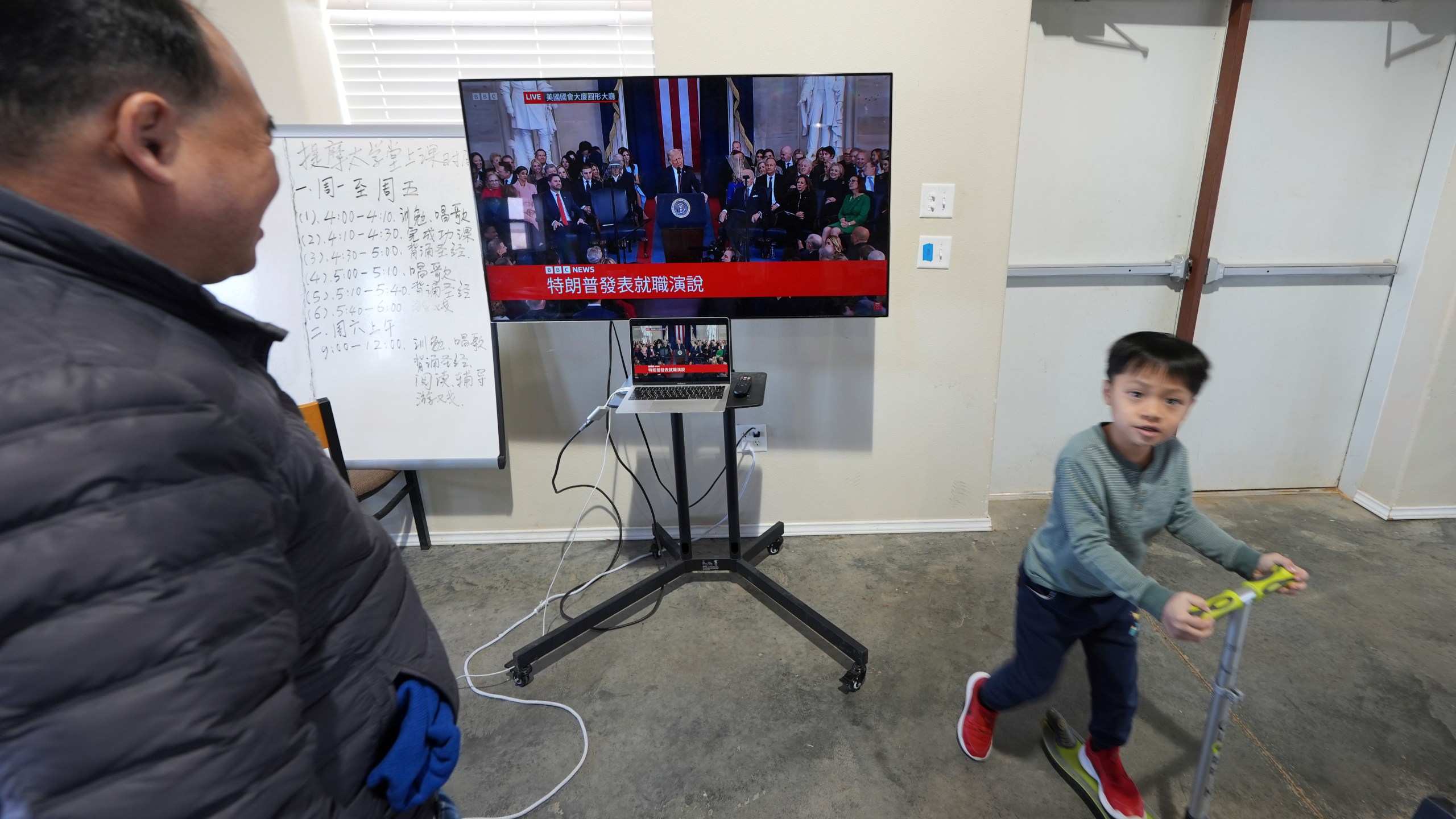 Pastor Pan Yongguang, left, part of a group of Chinese Christians resettled in Texas and awaiting final approval of their refugee status, watches a Chinese-captioned live broadcast of President Donald Trump's inauguration, Monday, Jan. 20, 2025, in Midland, Texas. (AP Photo/Rebecca Blackwell)