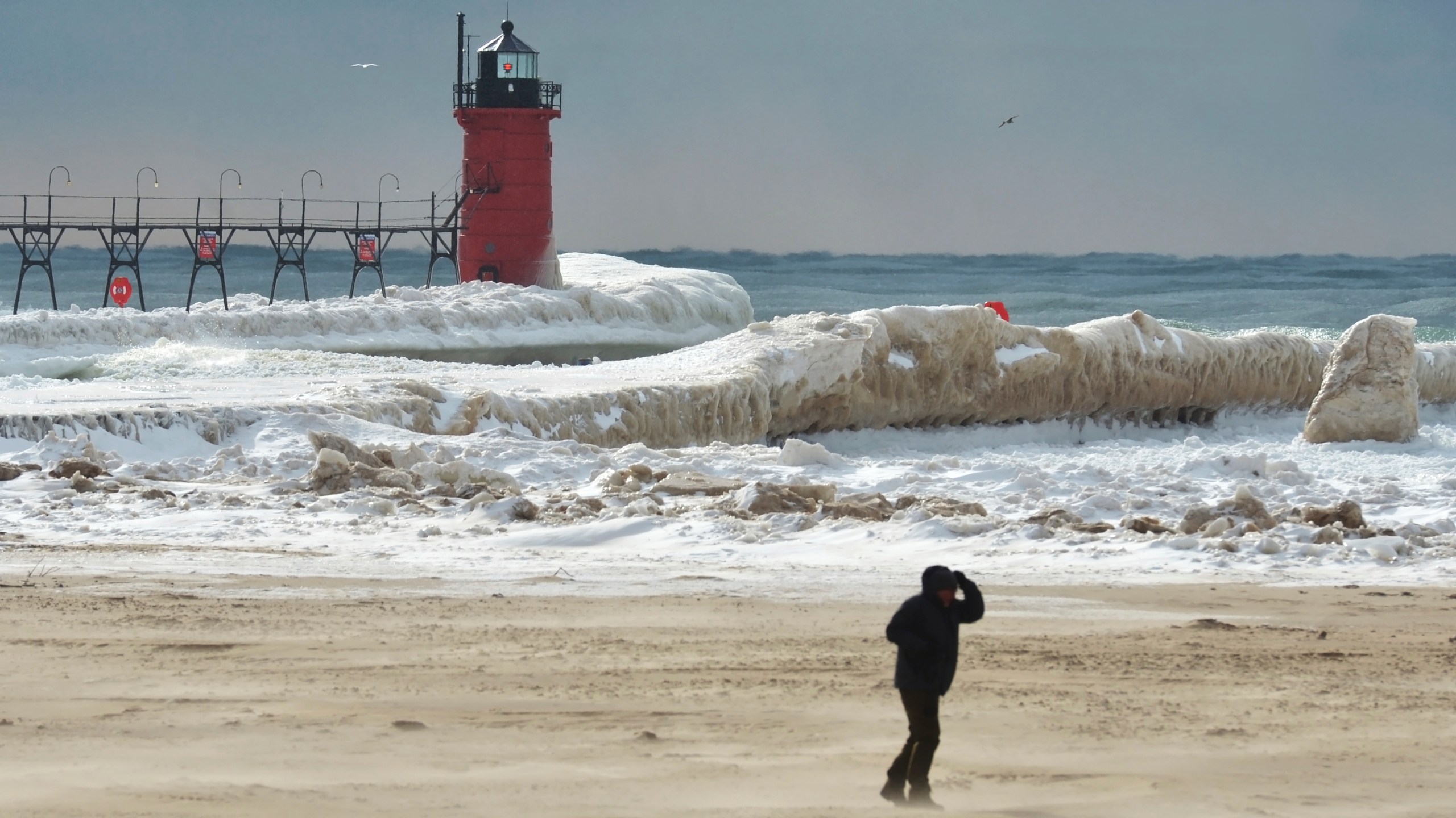 The sun breaks through overcast skies as ice forms along Lake Michigan and the South Haven Lighthouse Monday, Feb. 17, 2025, in South Haven, Mich. (Don Campbell/The Herald-Palladium via AP)