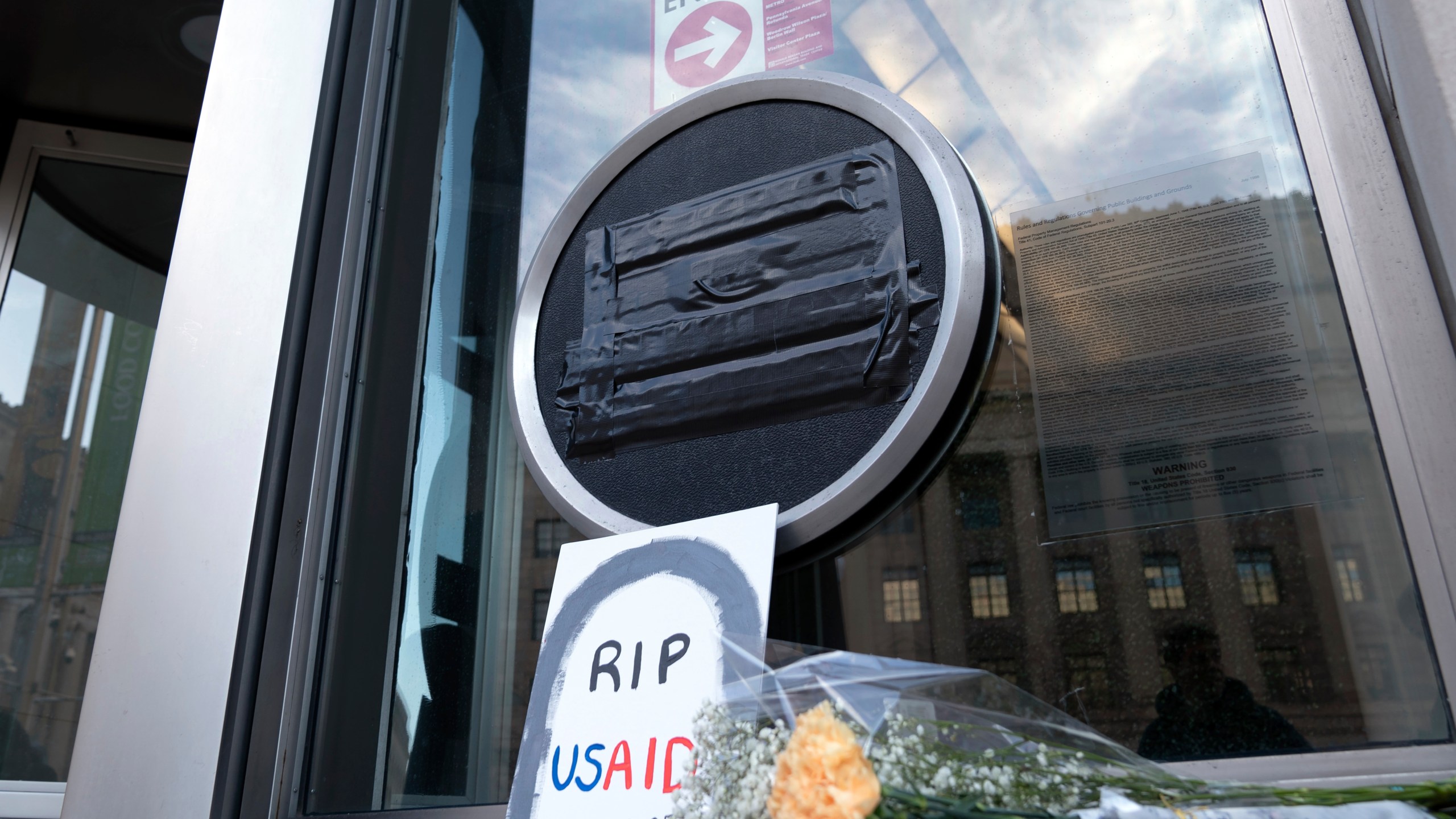 Flowers and a sign are placed outside the headquarters of the U.S. Agency for International Development, or USAID, Friday, Feb. 7, 2025, in Washington. (AP Photo/Jose Luis Magana)