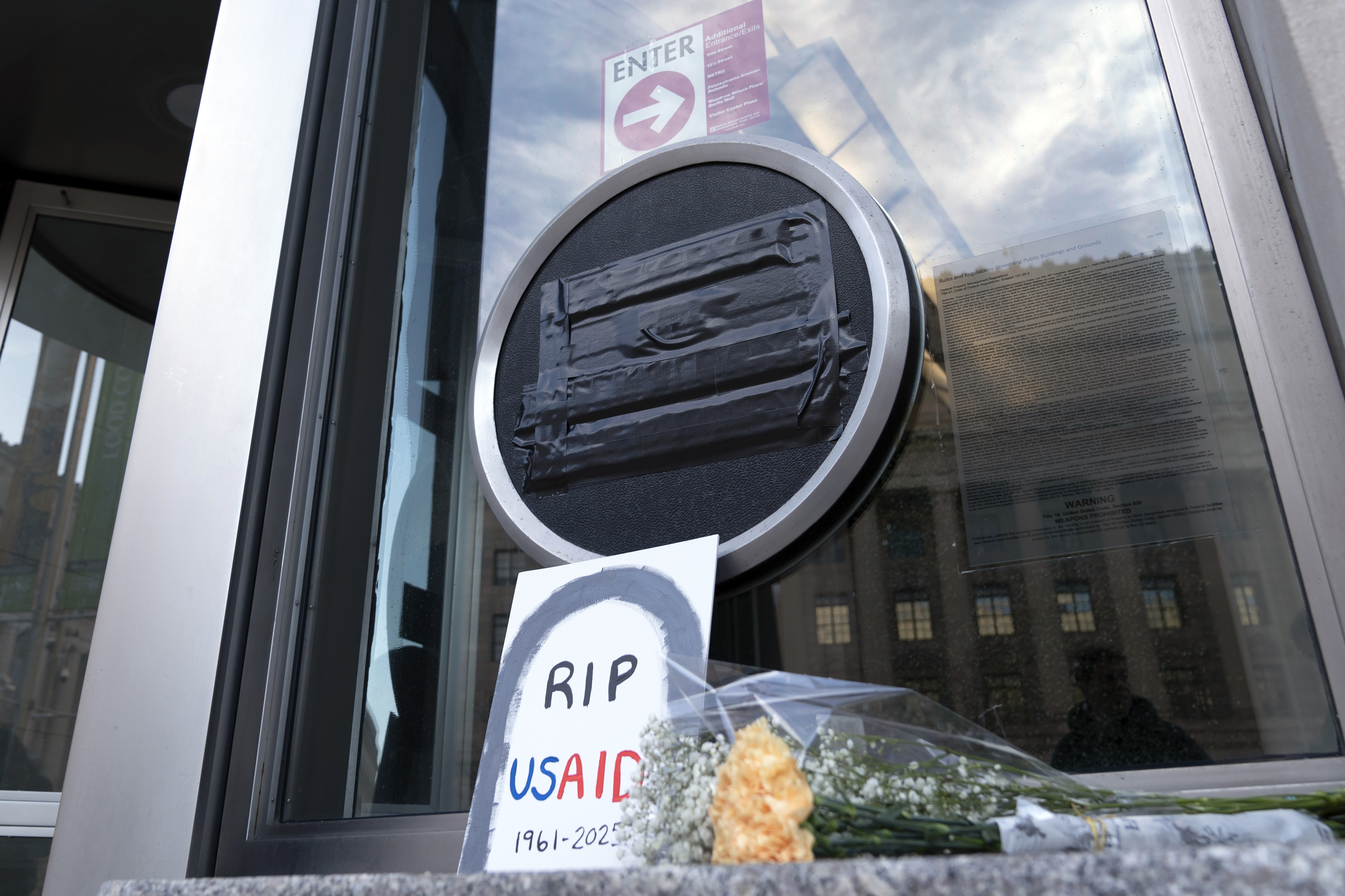 Flowers and a sign are placed outside the headquarters of the U.S. Agency for International Development, or USAID, Friday, Feb. 7, 2025, in Washington. (AP Photo/Jose Luis Magana)