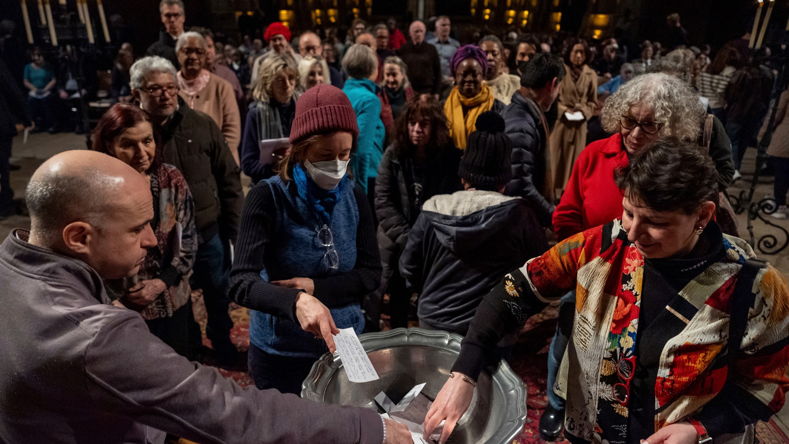 People place papers with their fears written down into a basin during an interfaith vigil for sanctuary at the Cathedral Church of St. John the Divine, Wednesday, Feb. 12, 2025, in New York. (AP Photo/Julia Demaree Nikhinson)