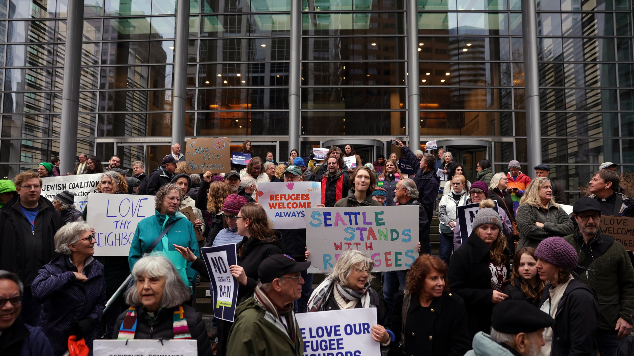 People hold signs as they gather outside the U.S. District Court after a federal judge blocked President Donald Trump's effort to halt the nation's refugee admissions system Tuesday, Feb. 25, 2025, in Seattle. (AP Photo/Ryan Sun)