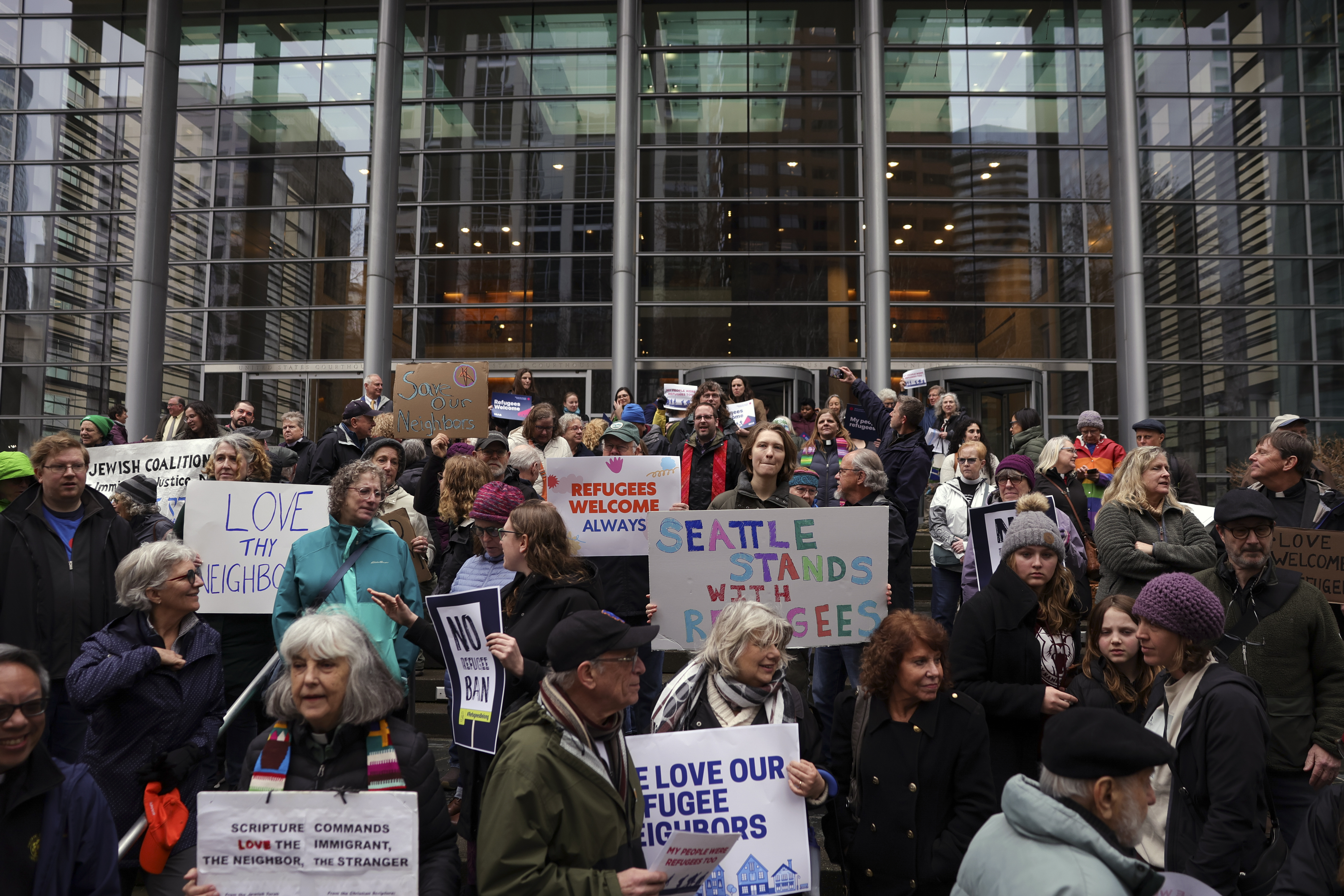 People hold signs as they gather outside the U.S. District Court after a federal judge blocked President Donald Trump's effort to halt the nation's refugee admissions system Tuesday, Feb. 25, 2025, in Seattle. (AP Photo/Ryan Sun)