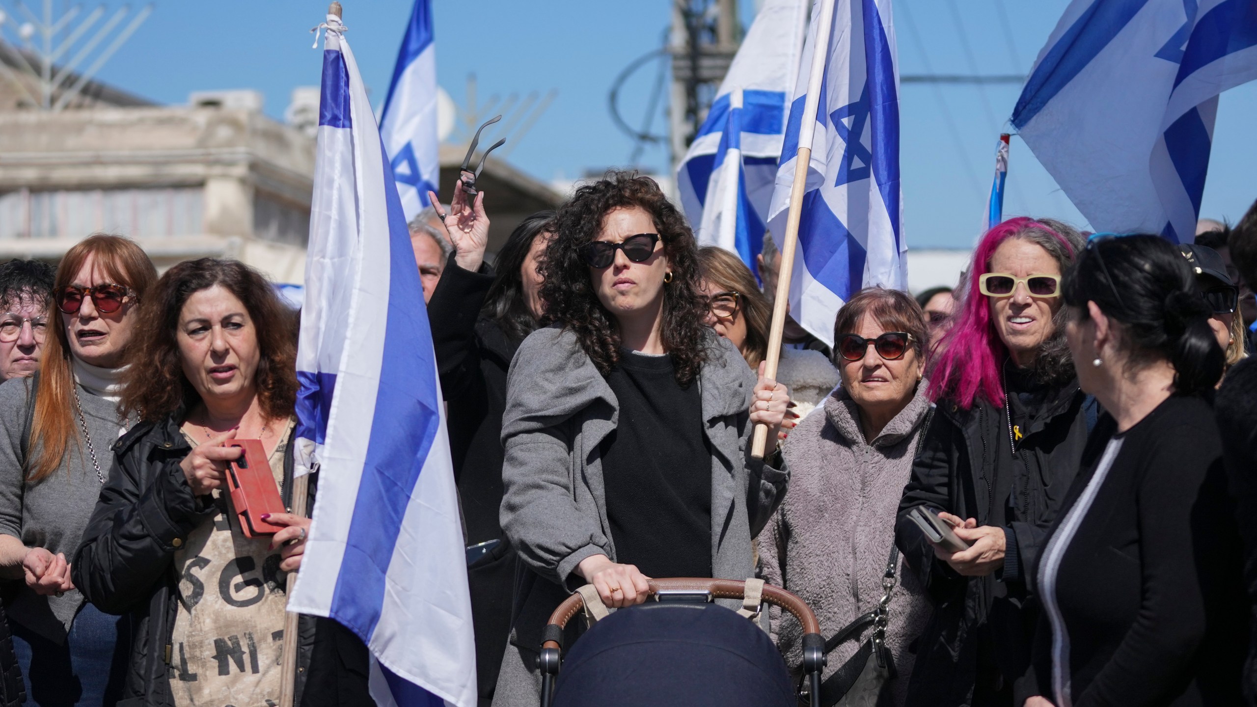 People wave Israeli flags before the funeral of former hostage Oded Lifshitz in Rishon Lezion, central Israel, on Tuesday, Feb. 25, 2025. Lifshitz was abducted by Hamas on Oct. 7, 2023, and his remains were returned from Gaza to Israel last week as part of a ceasefire with Hamas. (AP Photo/Maya Alleruzzo)