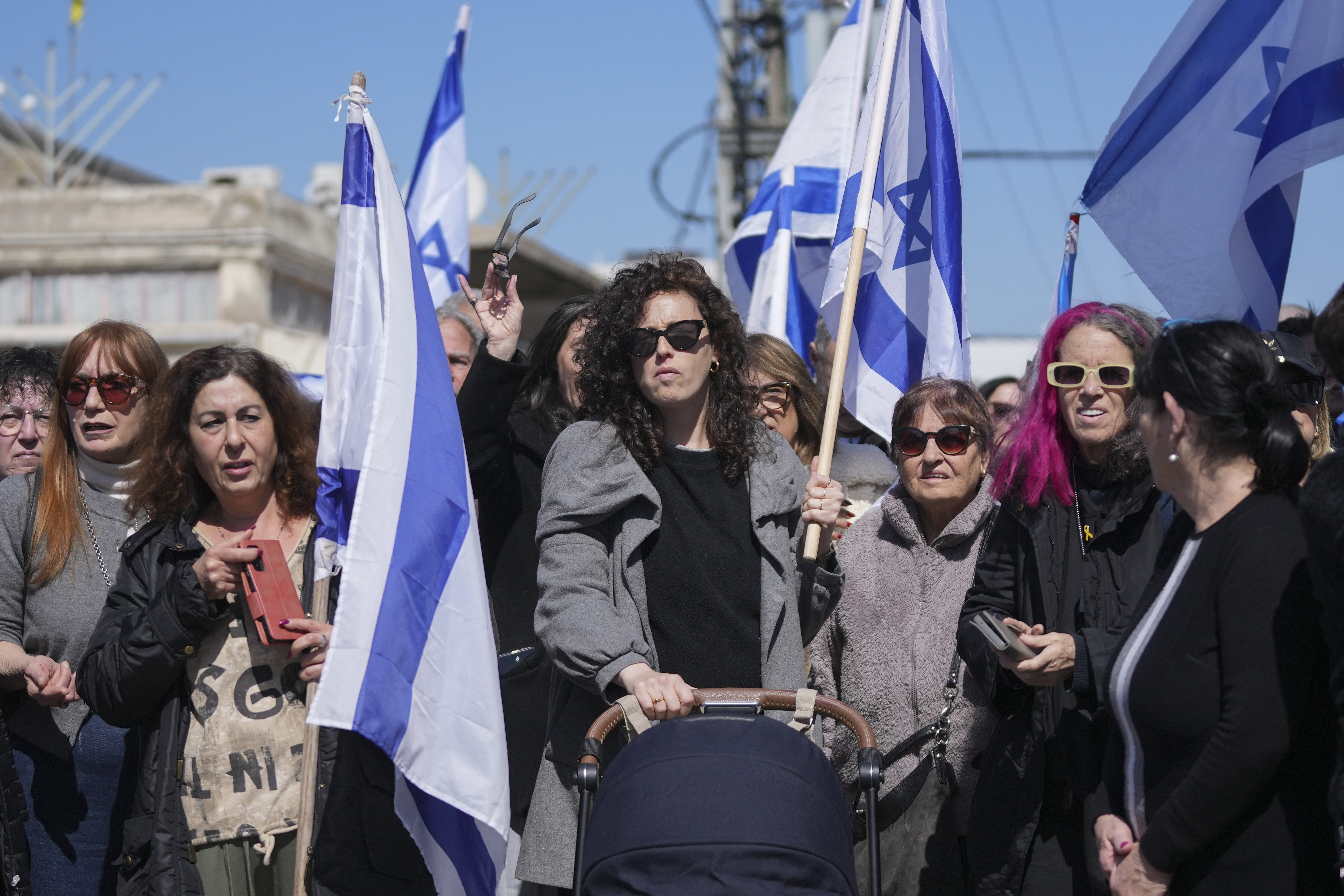 People wave Israeli flags before the funeral of former hostage Oded Lifshitz in Rishon Lezion, central Israel, on Tuesday, Feb. 25, 2025. Lifshitz was abducted by Hamas on Oct. 7, 2023, and his remains were returned from Gaza to Israel last week as part of a ceasefire with Hamas. (AP Photo/Maya Alleruzzo)